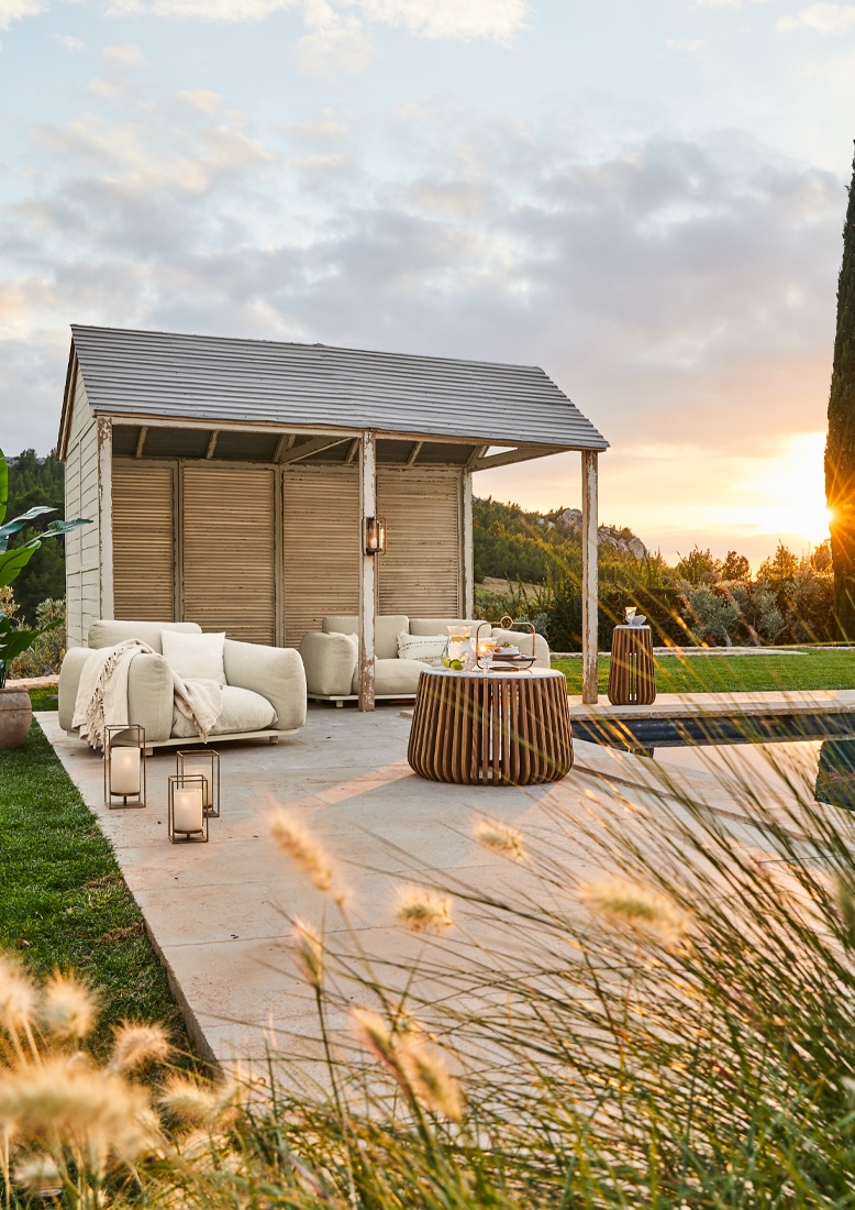 Pavillon de jardin blanc avec mobilier beige et table en bois sur terrasse au coucher du soleil