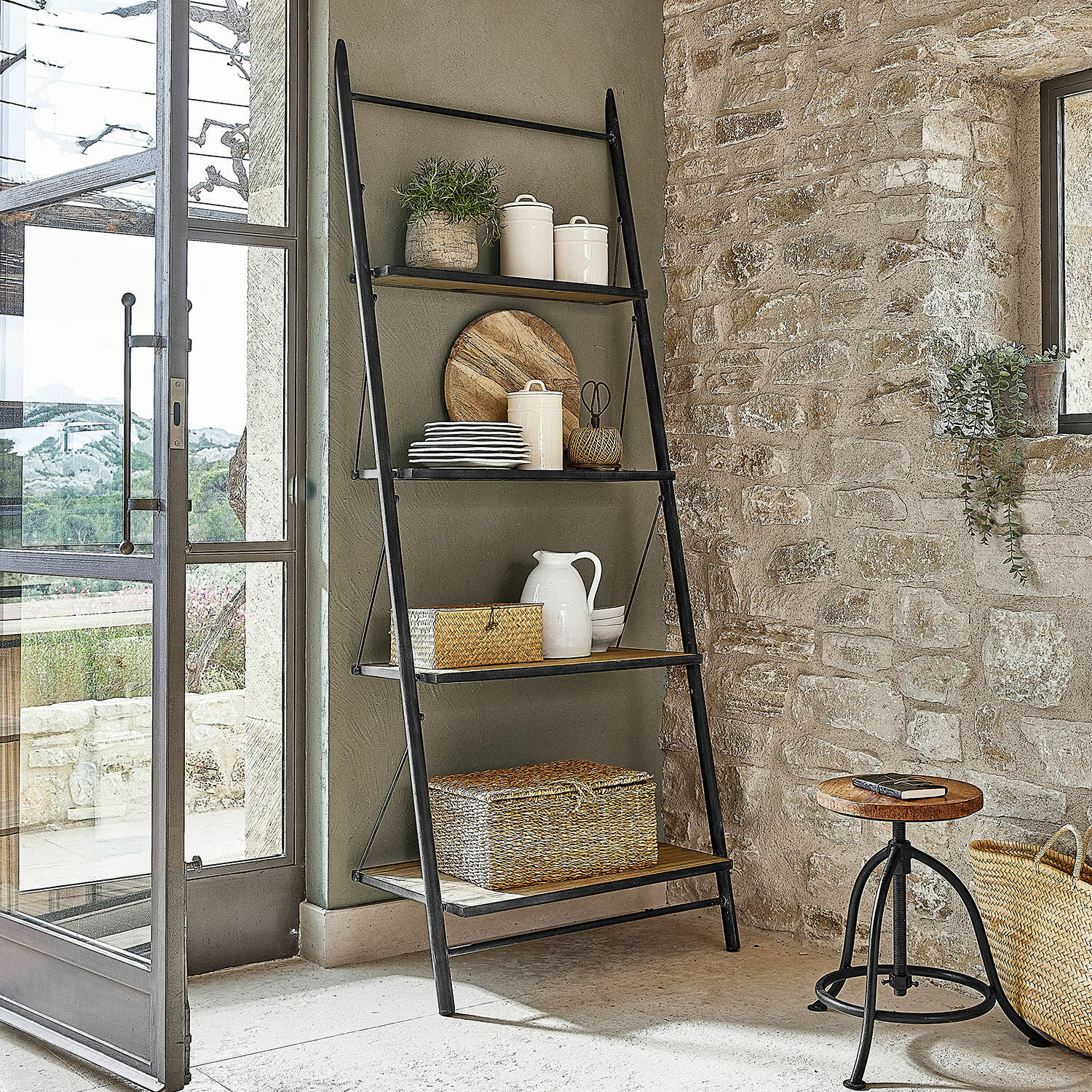 Étagère Greenbriar Échelle noire en métal avec étagères en bois et décorations dans un intérieur rustique en pierre