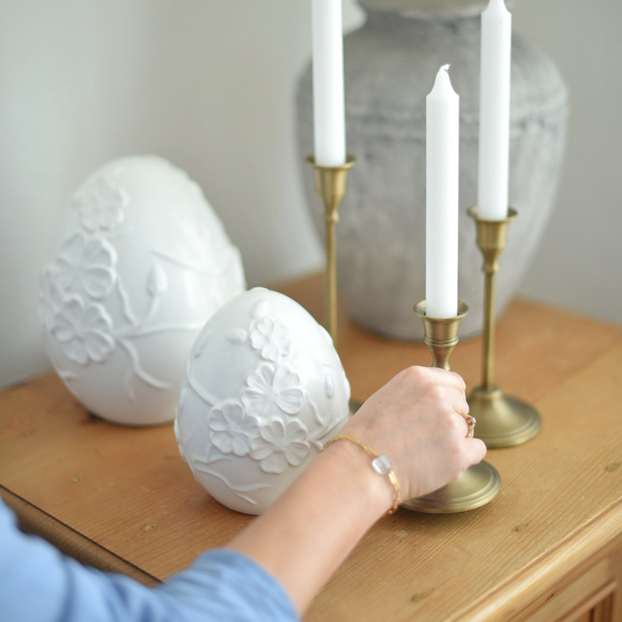 Œufs décoratifs en céramique blanche avec relief floral sur table en bois près de chandeliers en laiton
