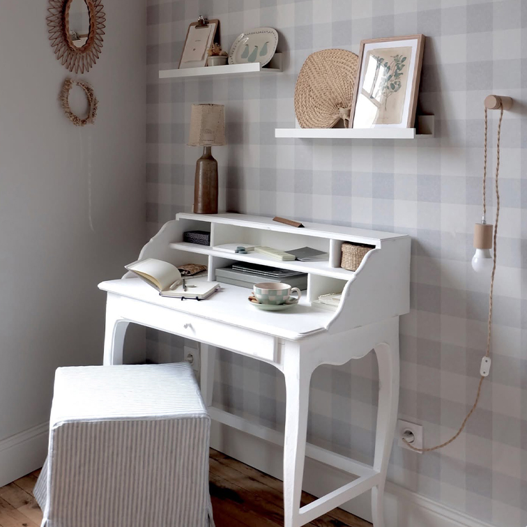 Bureau secrétaire blanc en bois avec étagères, lampe et tasse dans une pièce chaleureuse à papier peint à carreaux