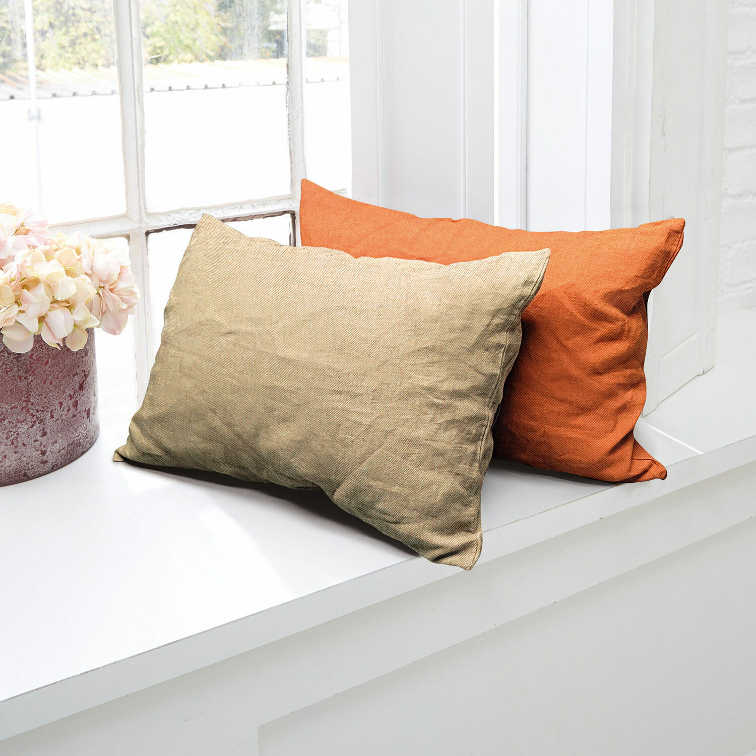 Lot de 2 housses de coussins Balesta Deux coussins décoratifs en tissu beige et orange posés sur un rebord de fenêtre blanc