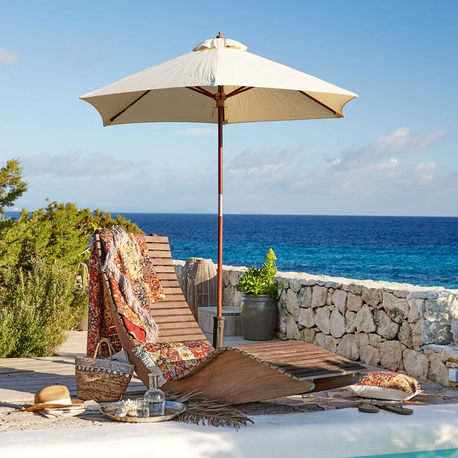 Chaise longue à bascule Wenham Chaise longue en bois avec parasol crème et plaid coloré au bord de la piscine face à la mer