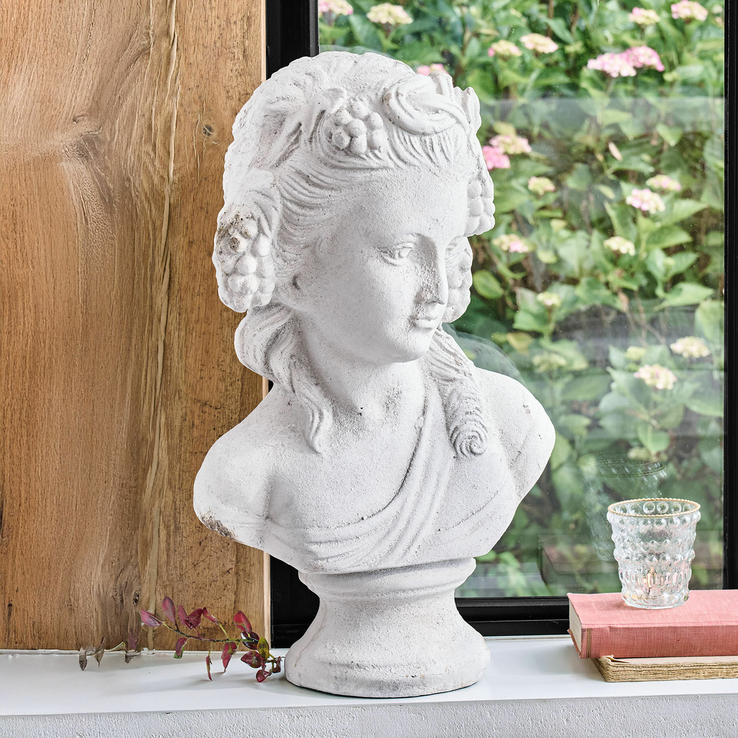 Buste Sanoria Buste blanc en pierre décorative représentant une femme avec des détails floraux posé sur un rebord de fenêtre