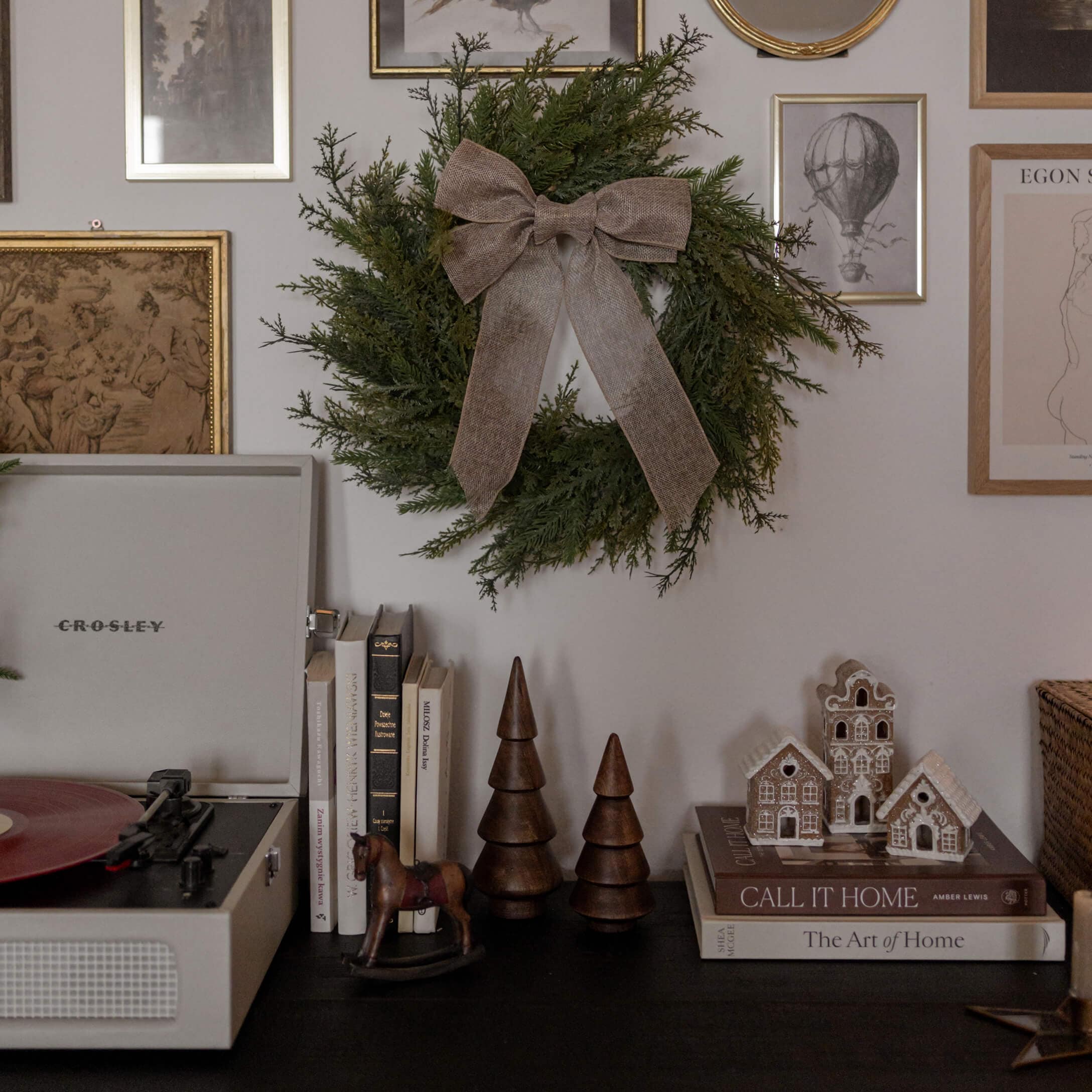 Couronne verte décorative avec un nœud marron suspendue au mur au-dessus d'une table noire avec livres et décorations