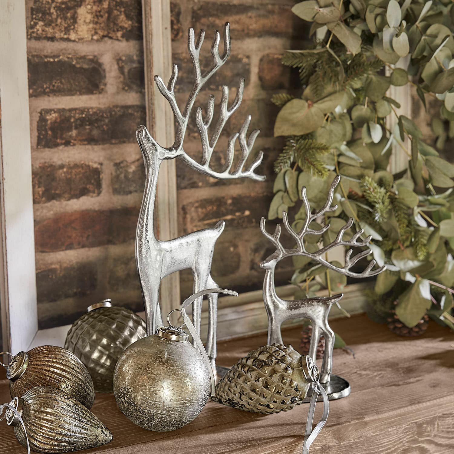 Lot de 2 rennes décoratifs Zerlay Figurines de rennes argentées et décorations de Noël posées sur une table en bois avec feuillage vert