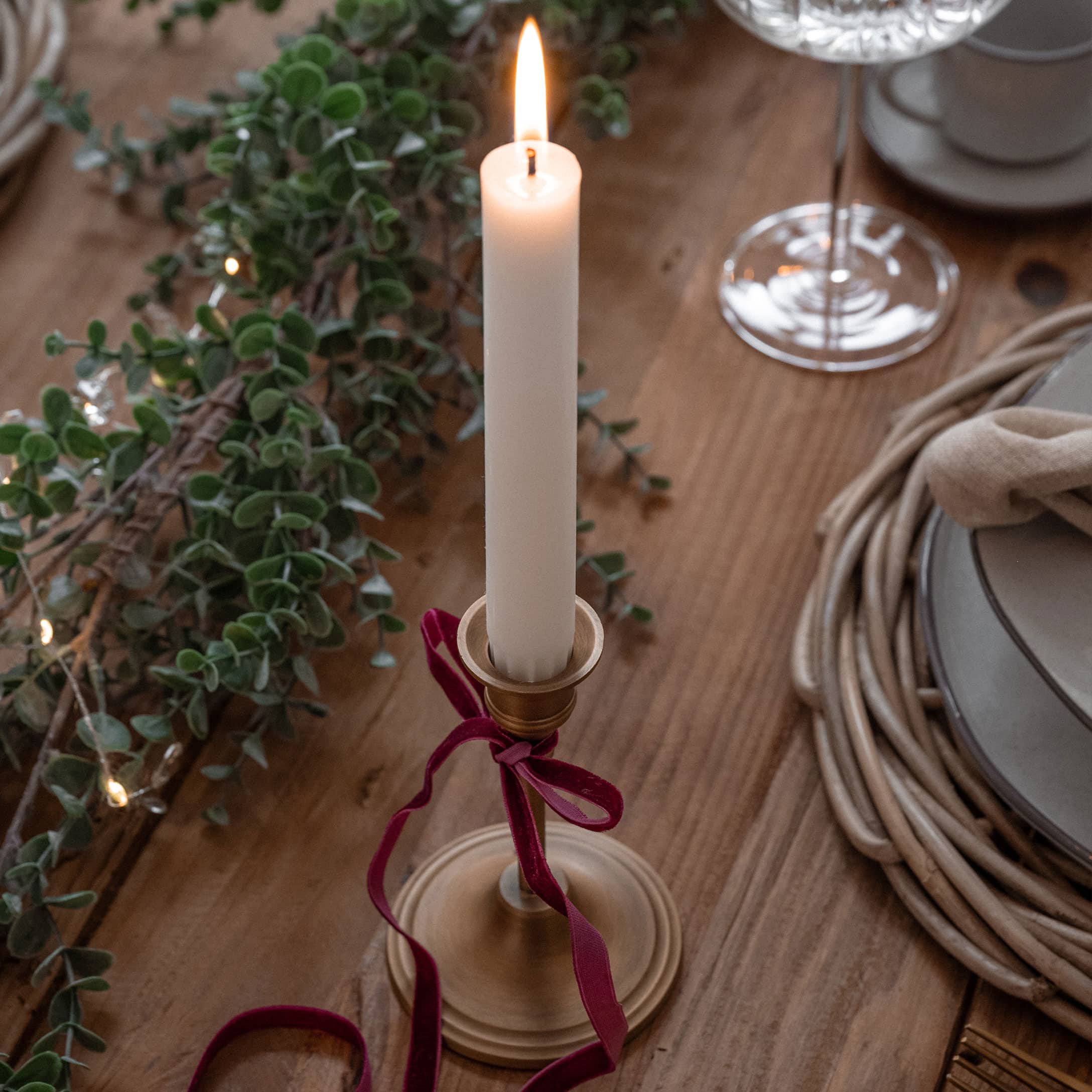 Bougeoir en métal doré avec une bougie blanche et un ruban bordeaux sur une table en bois décorée pour Noël