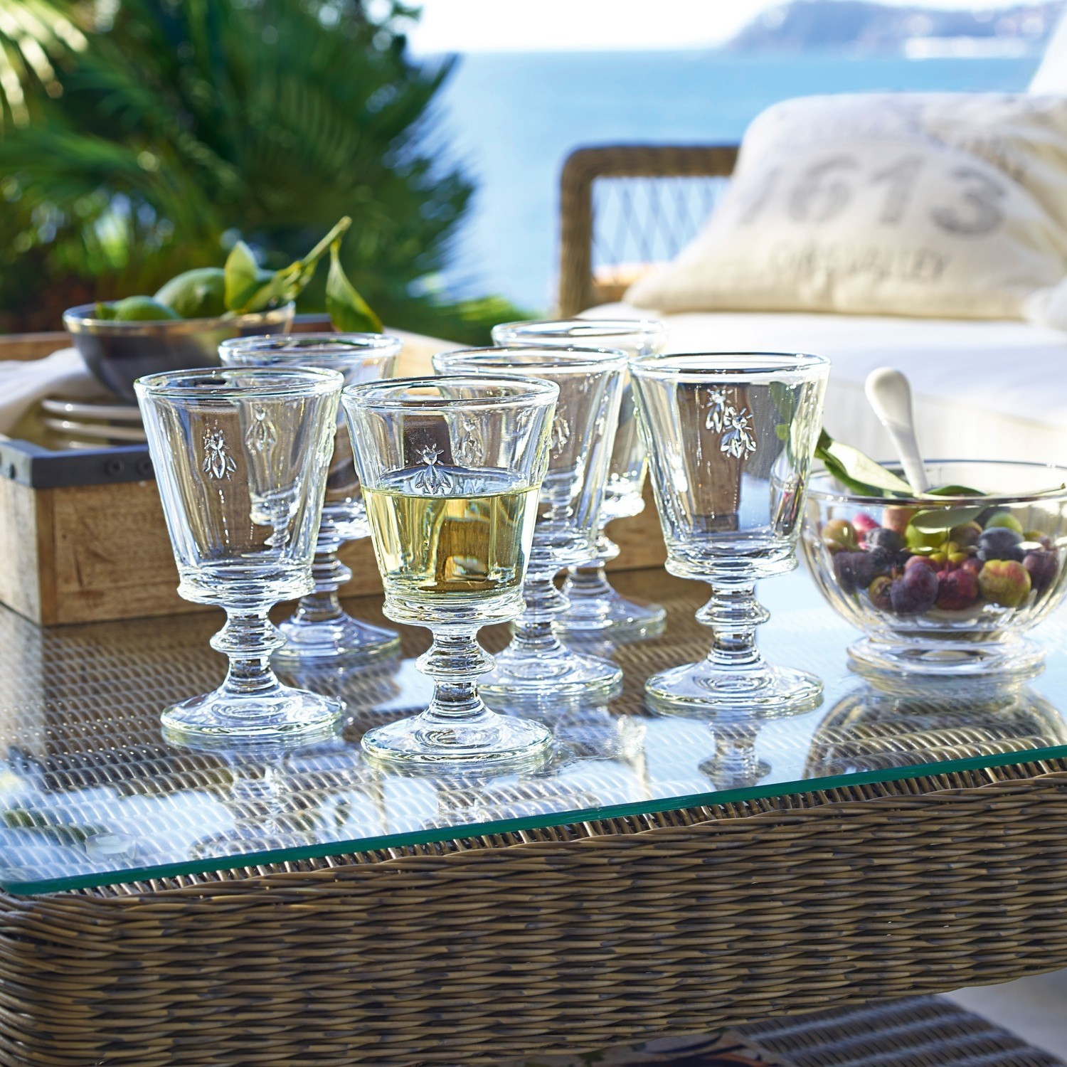 Lot de 6 verres à vin Puttigny Ensemble de six verres en verre avec motif d'insecte sur table en verre sur terrasse avec vue sur la mer