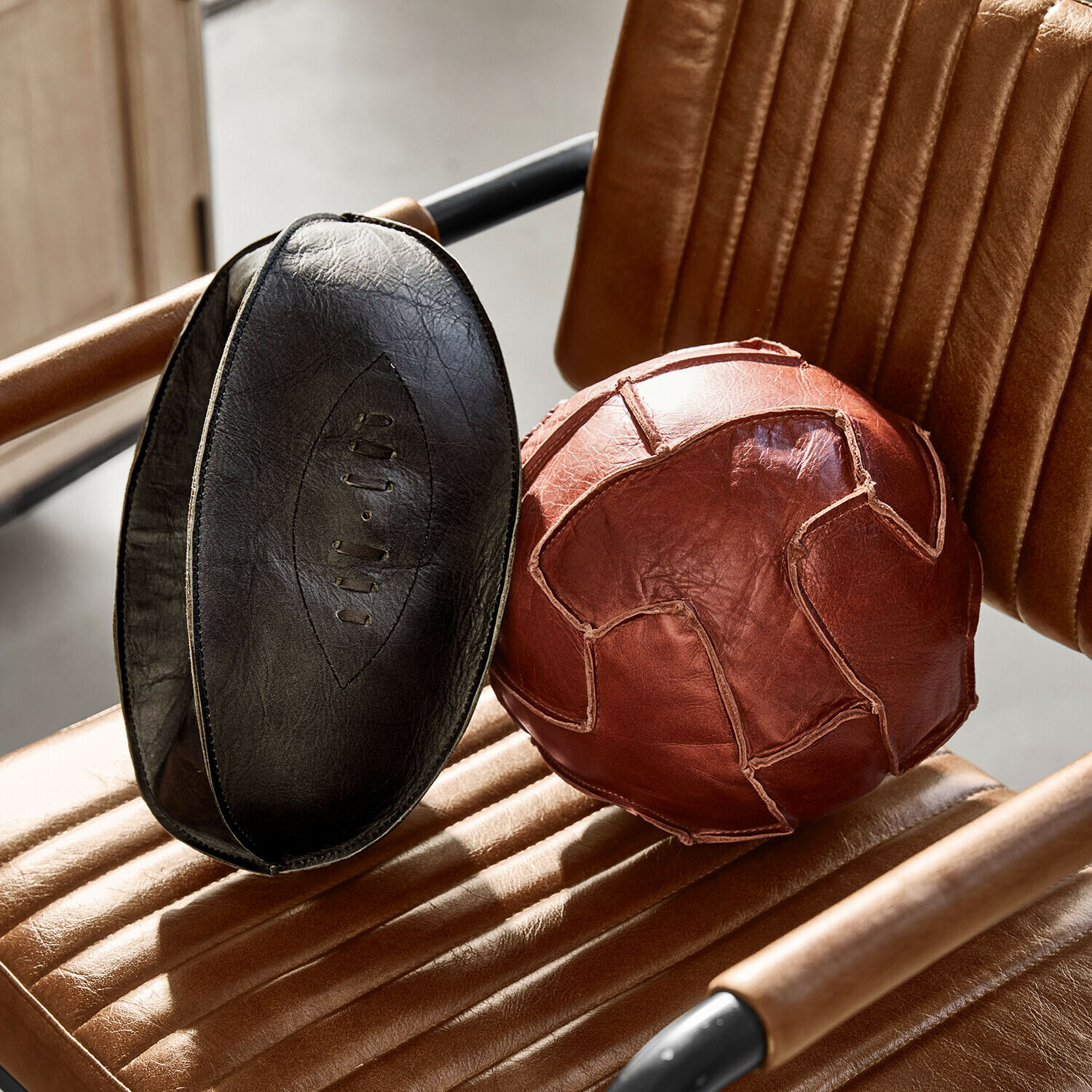 Set de 2 balles décoratives Awanian Ballon d'exercice en cuir naturel marron et noir posé sur un fauteuil en cuir marron
