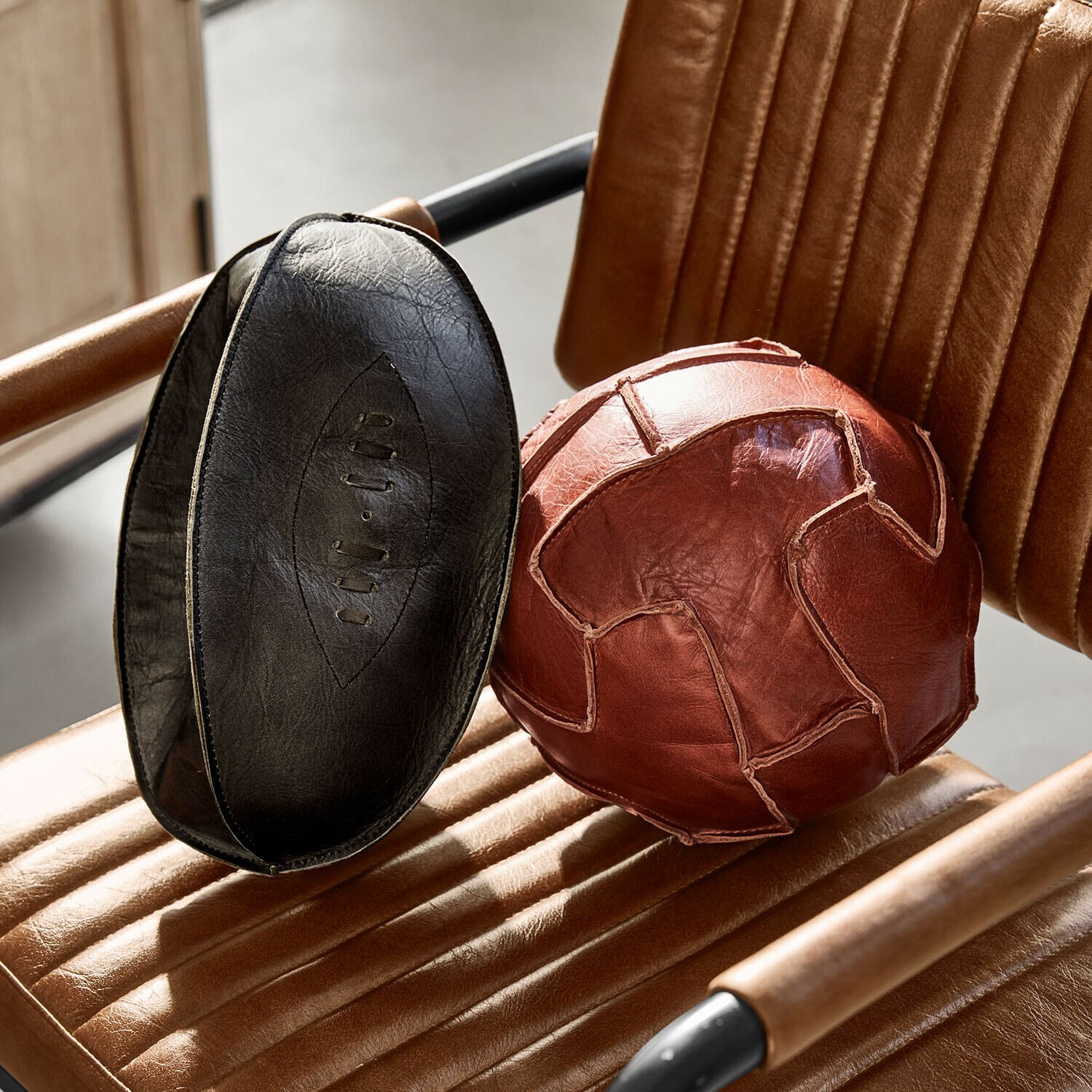 Set de 2 balles décoratives Awanian Ballon d'exercice en cuir naturel marron et noir posé sur un fauteuil en cuir marron