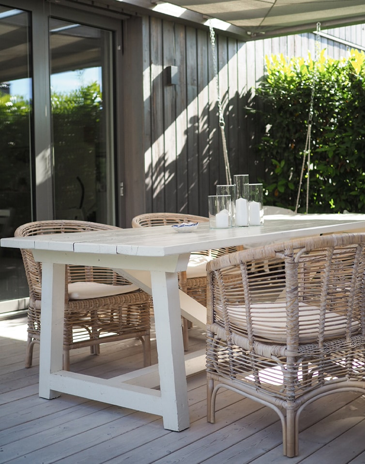 Table de jardin en bois blanc avec chaises en rotin naturel et bougies sur terrasse ensoleillée