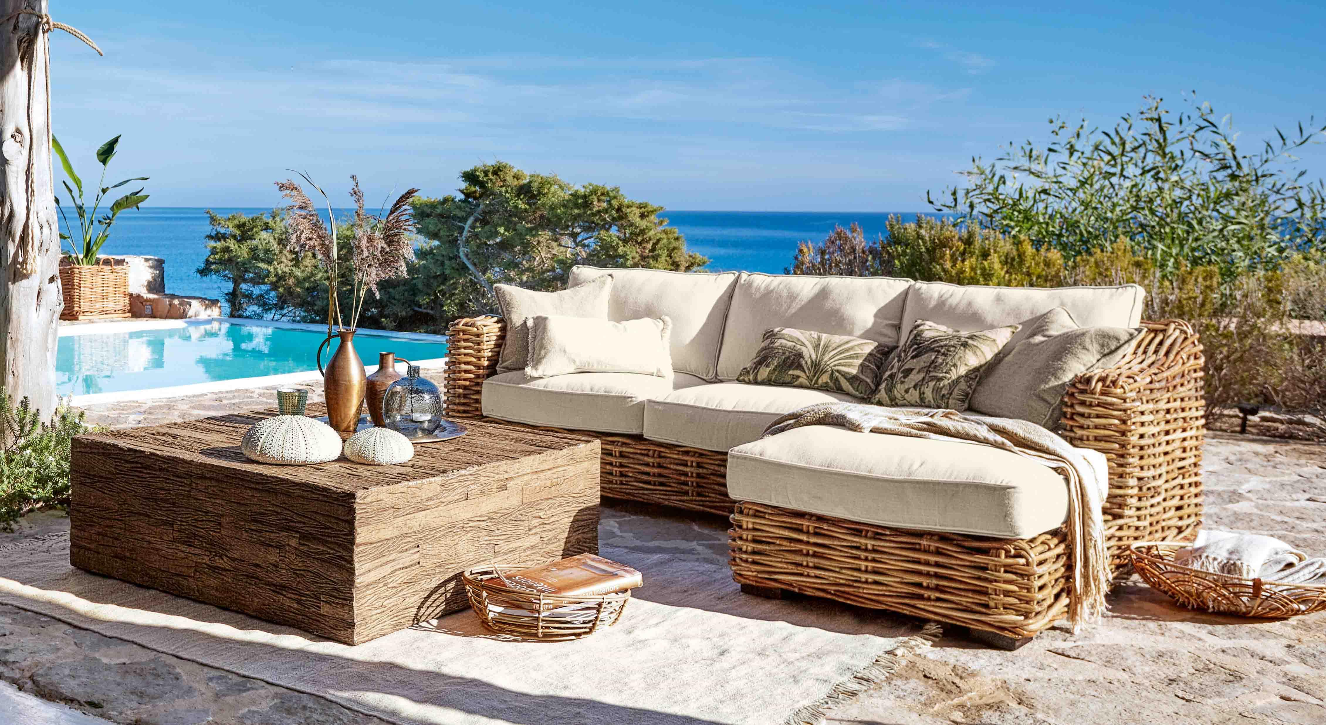 Ensemble de meubles d'extérieur en rotin avec coussins crème près d'une piscine face à la mer