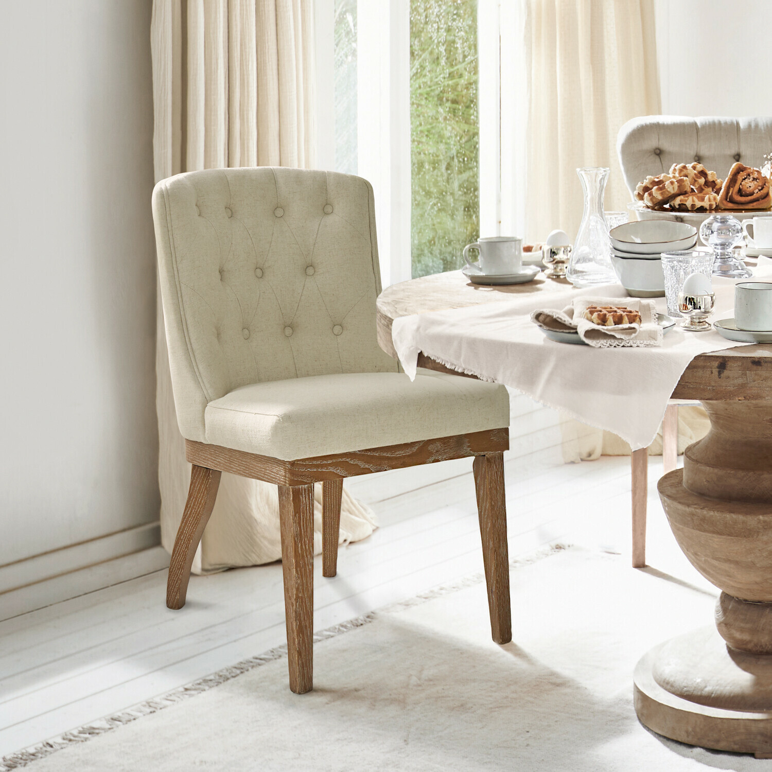 Chaise Fairwyn Chaise rembourrée beige avec pieds en bois près d'une table à manger dressée avec vaisselle et pâtisseries