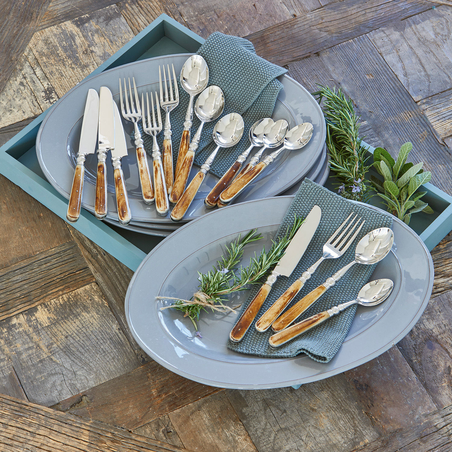 Couverts Bigeste Service de couverts avec manches en bois sur assiettes grises avec serviettes vertes et herbes fraîches