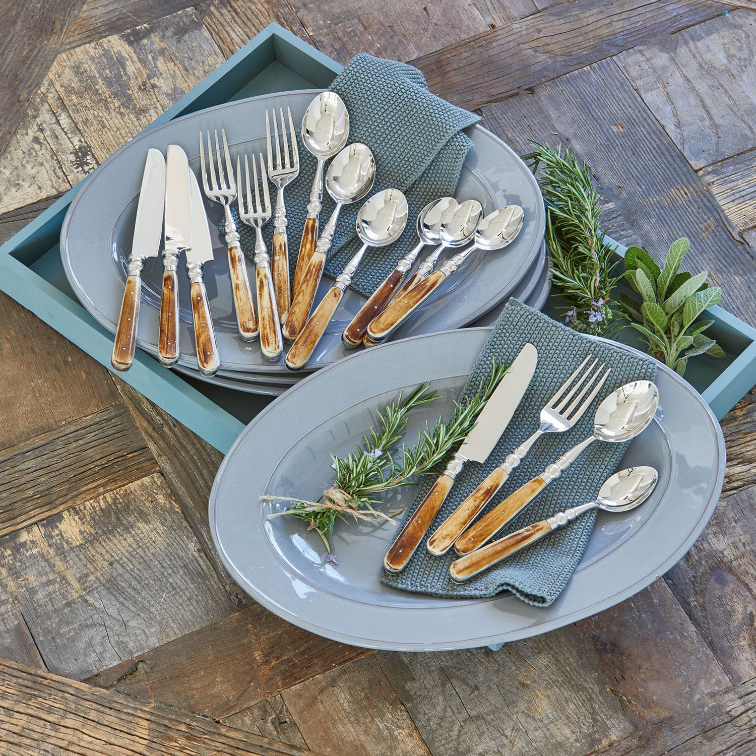 Couverts Bigeste Service de couverts avec manches en bois sur assiettes grises avec serviettes vertes et herbes fraîches
