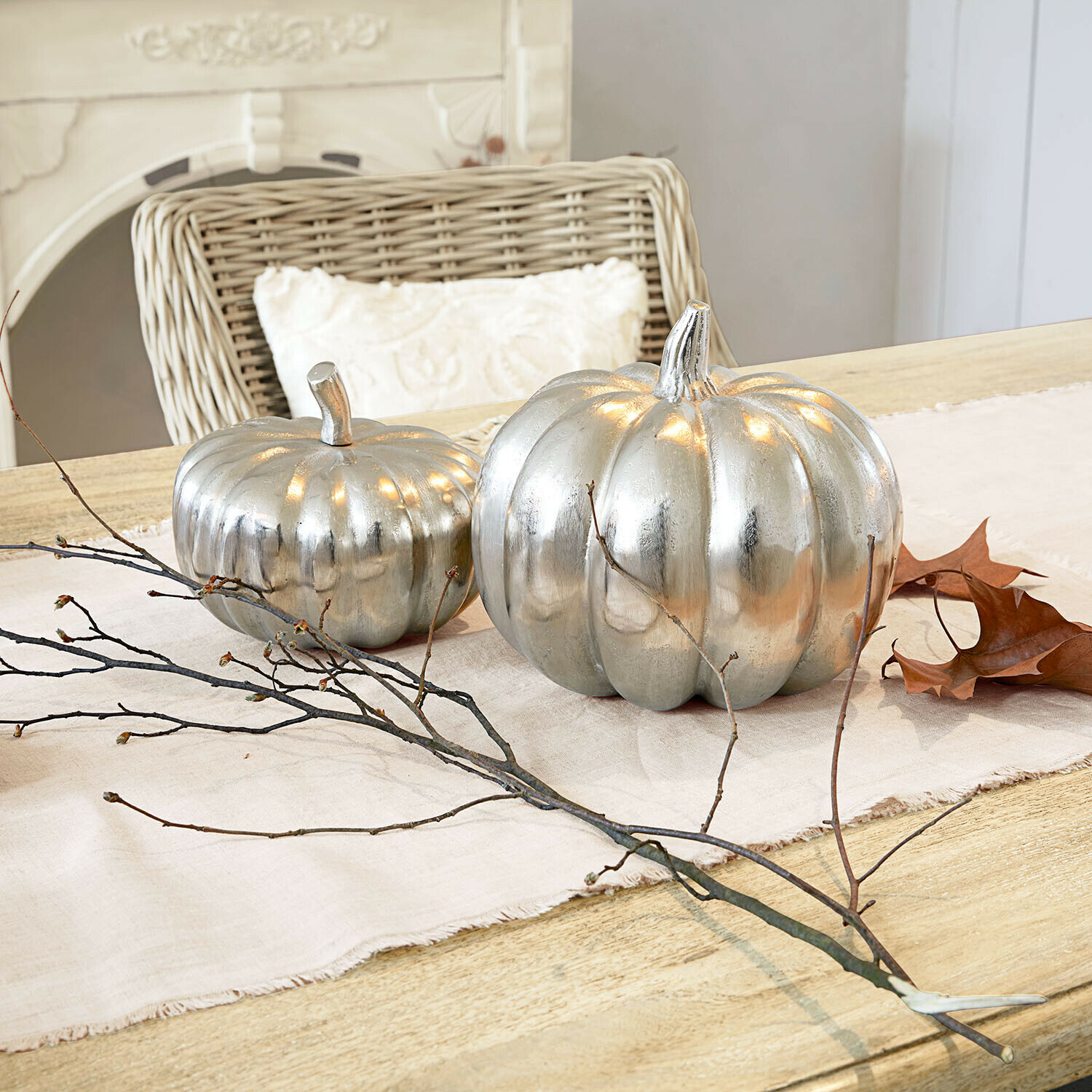 Lot de 2 citrouilles décoratives Alérisse Deux citrouilles décoratives en métal argenté sur une nappe claire avec branches et feuilles sèches