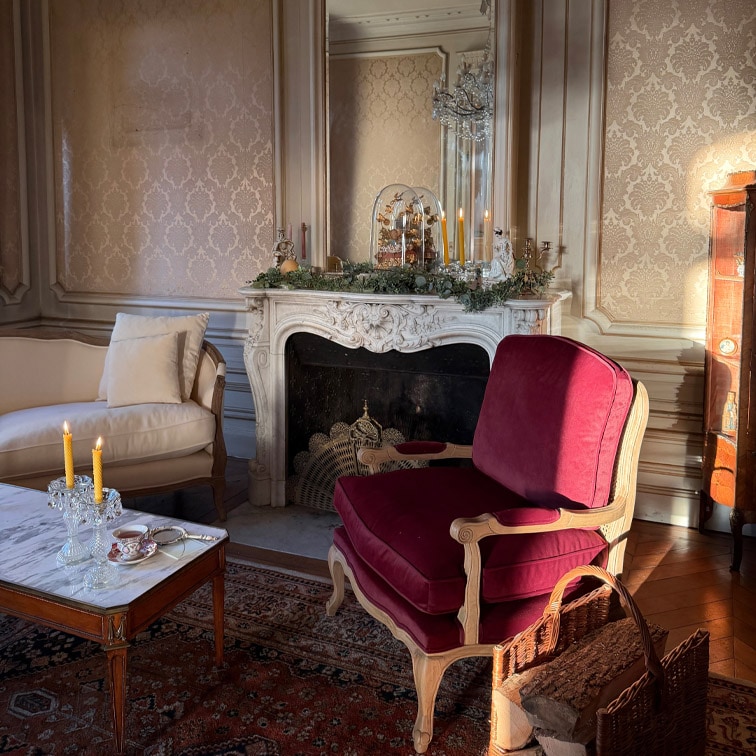 Salon classique avec fauteuil bordeaux en bois et table en marbre avec bougies allumées