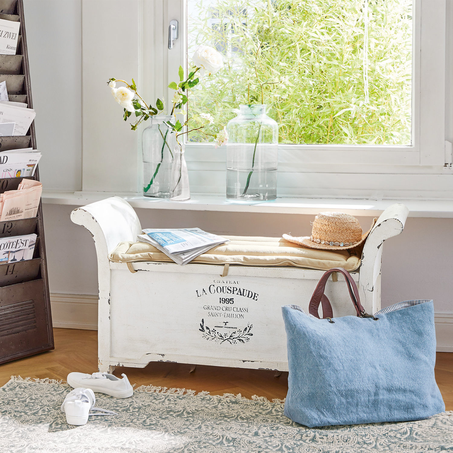 Banc Andance Banc en bois blanc avec coussin, chapeau et sac bleu devant une fenêtre avec des fleurs