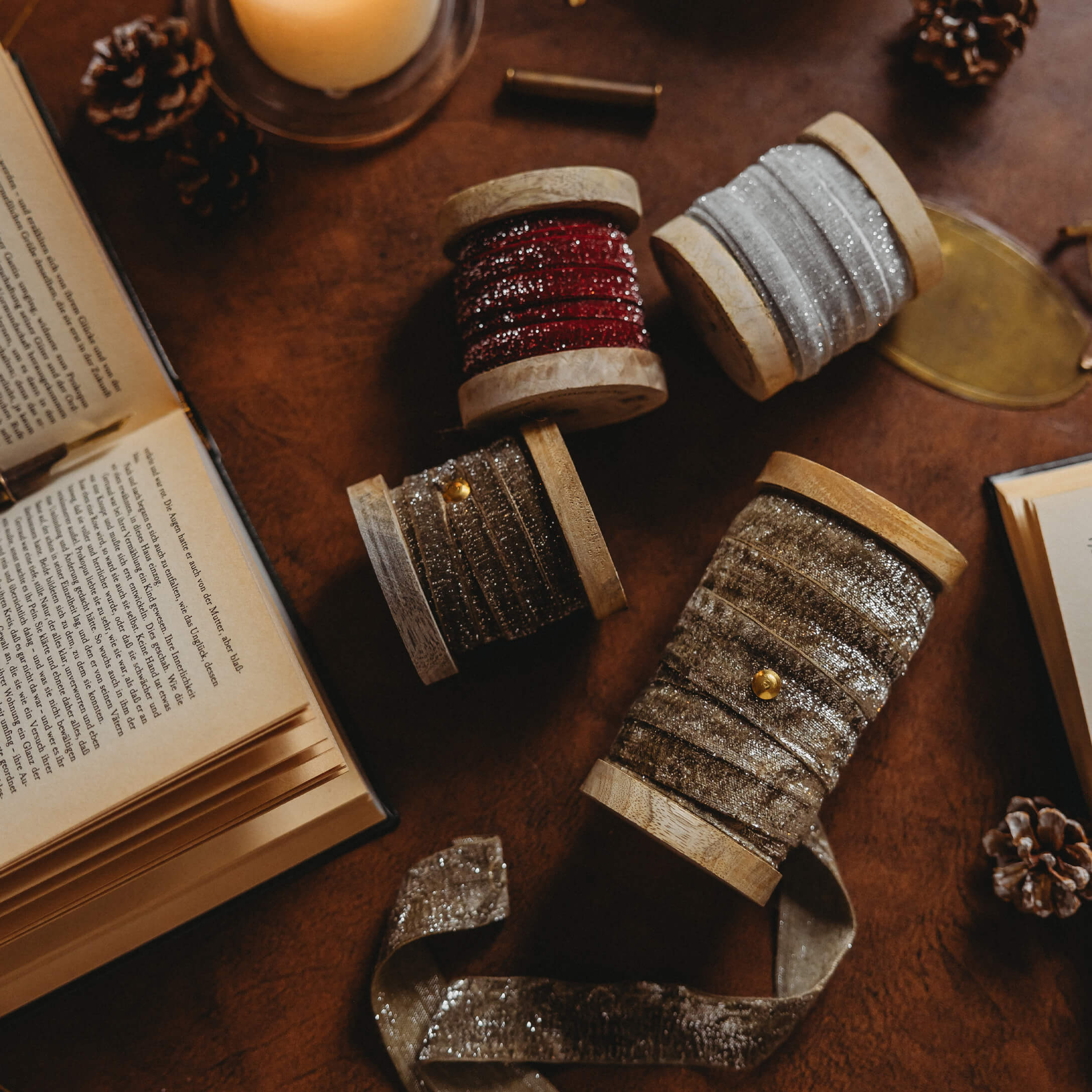 Bobines en bois avec rubans brillants rouges, argentés et dorés sur une table avec des livres ouverts