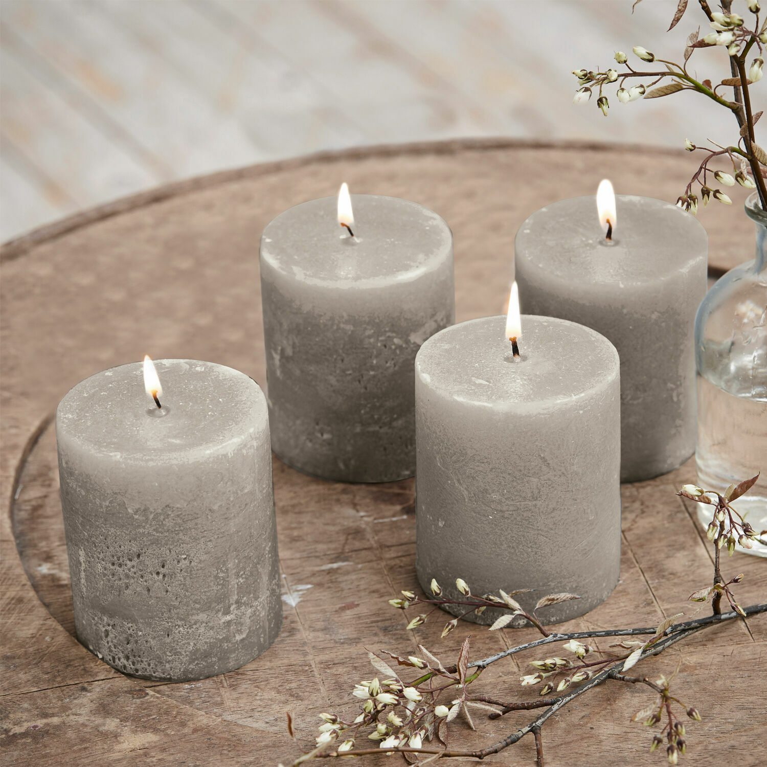 Lot de 4 bougies Virrans Ensemble de quatre bougies en cire grises sur une table en bois avec décoration florale, ambiance cosy