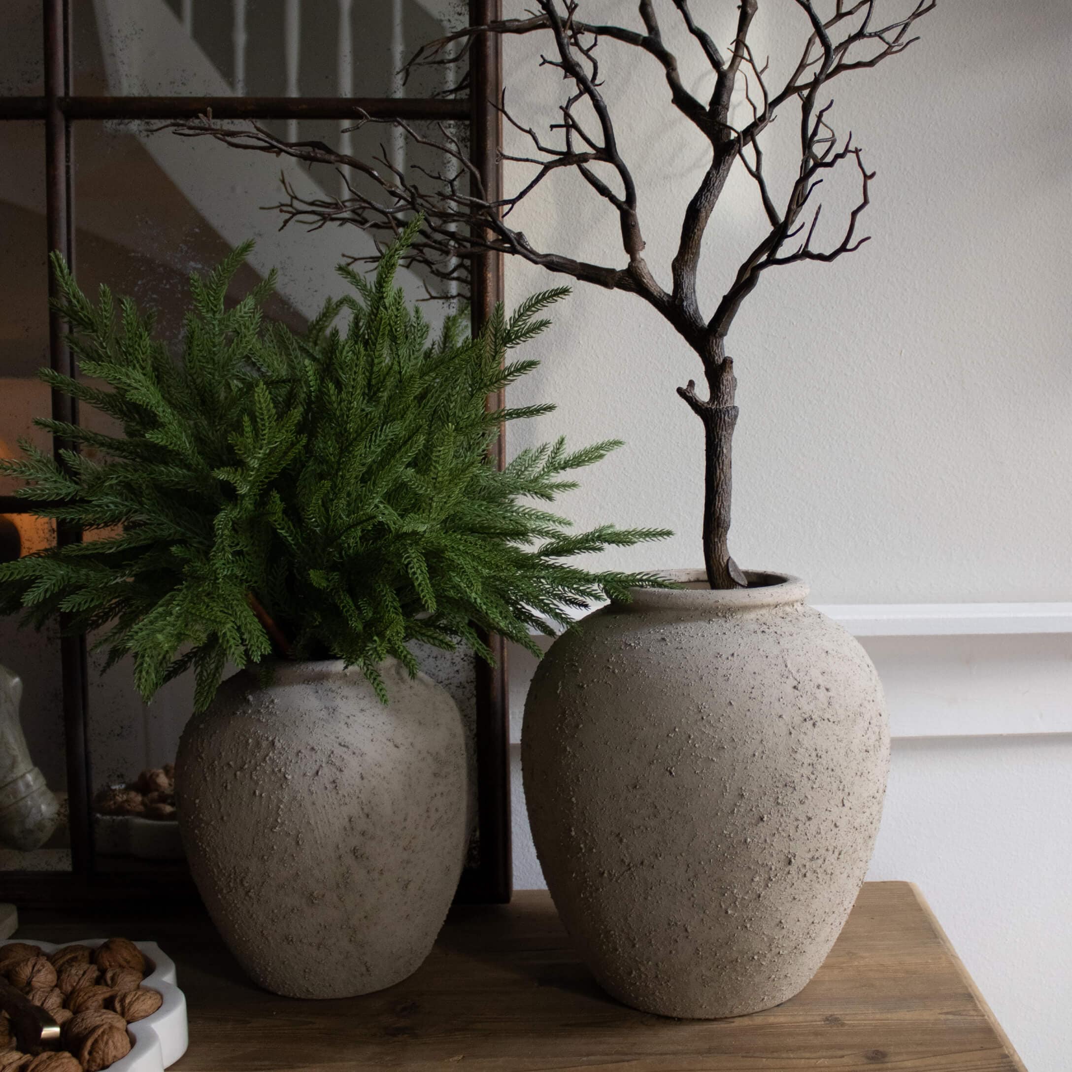 Deux vases décoratifs en pierre grise sur une table en bois avec feuillage vert et branches sèches