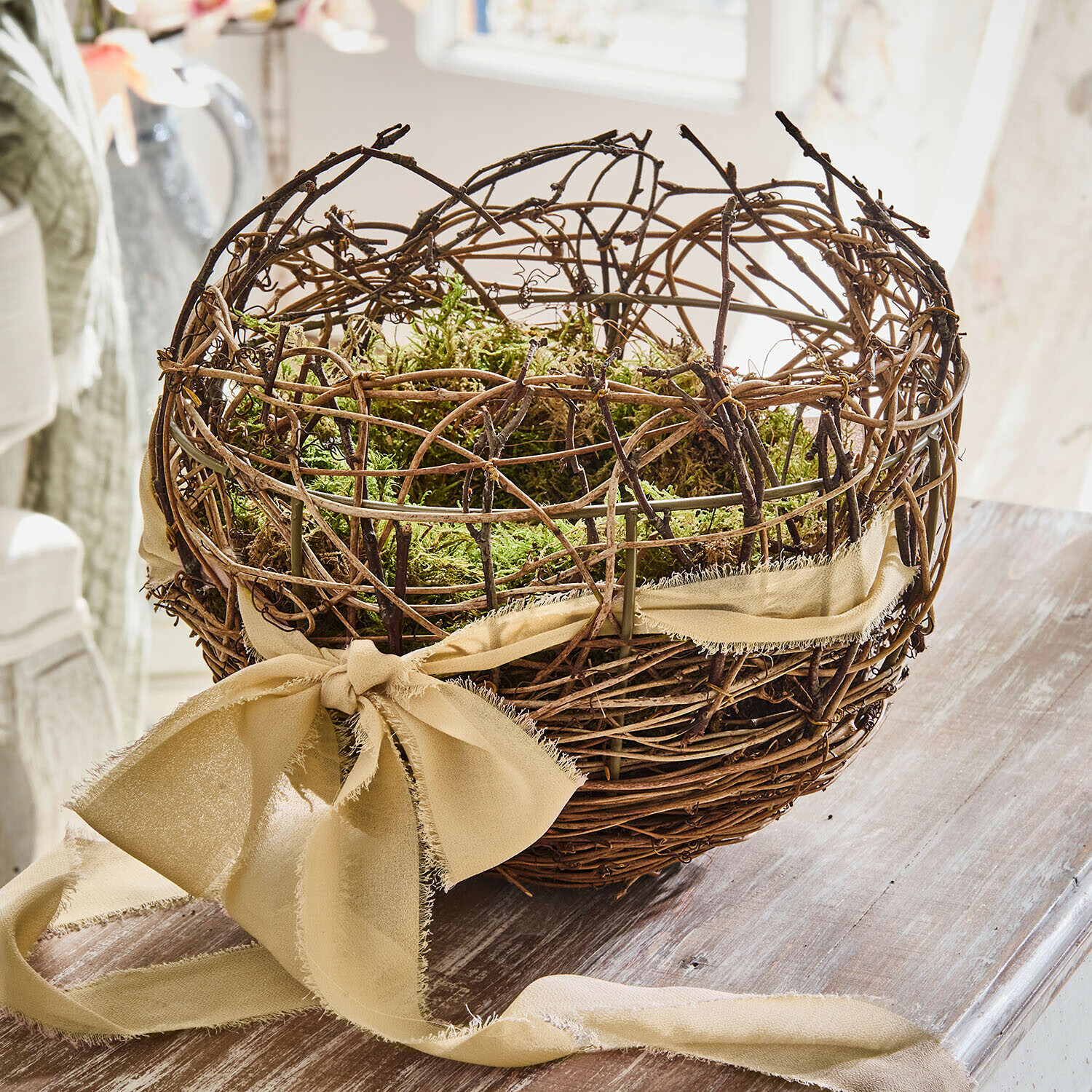 Panier Avenra Panier décoratif en branches avec mousse verte et ruban beige sur table en bois pour décoration intérieure
