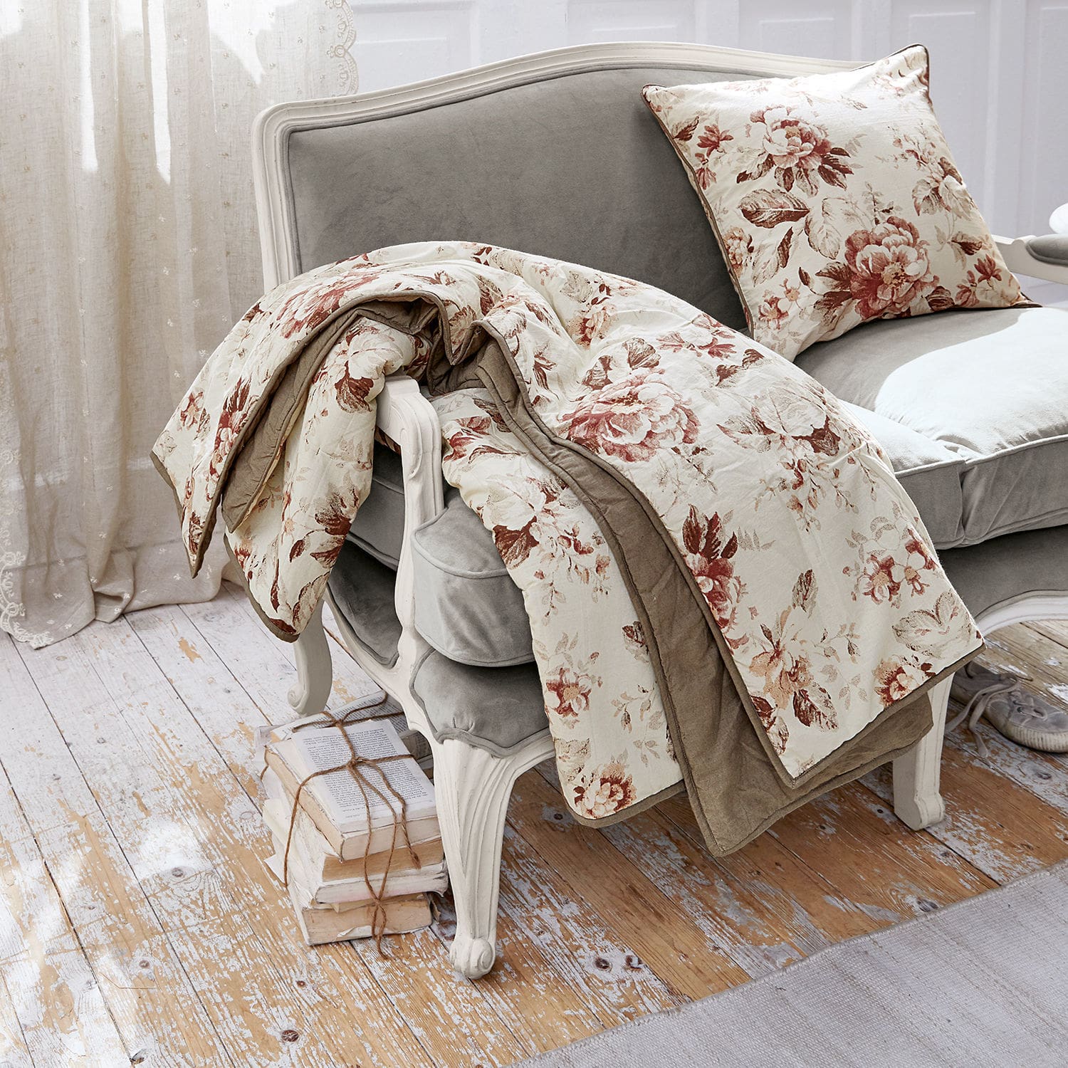 Courtepointe Corbusier Plaid et coussin à motif floral beige et marron sur un canapé gris style vintage dans un intérieur lumineux