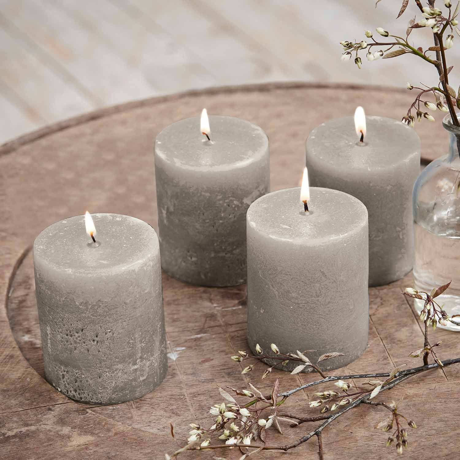 Ensemble de quatre bougies cylindriques grises en cire sur une table en bois avec décoration florale
