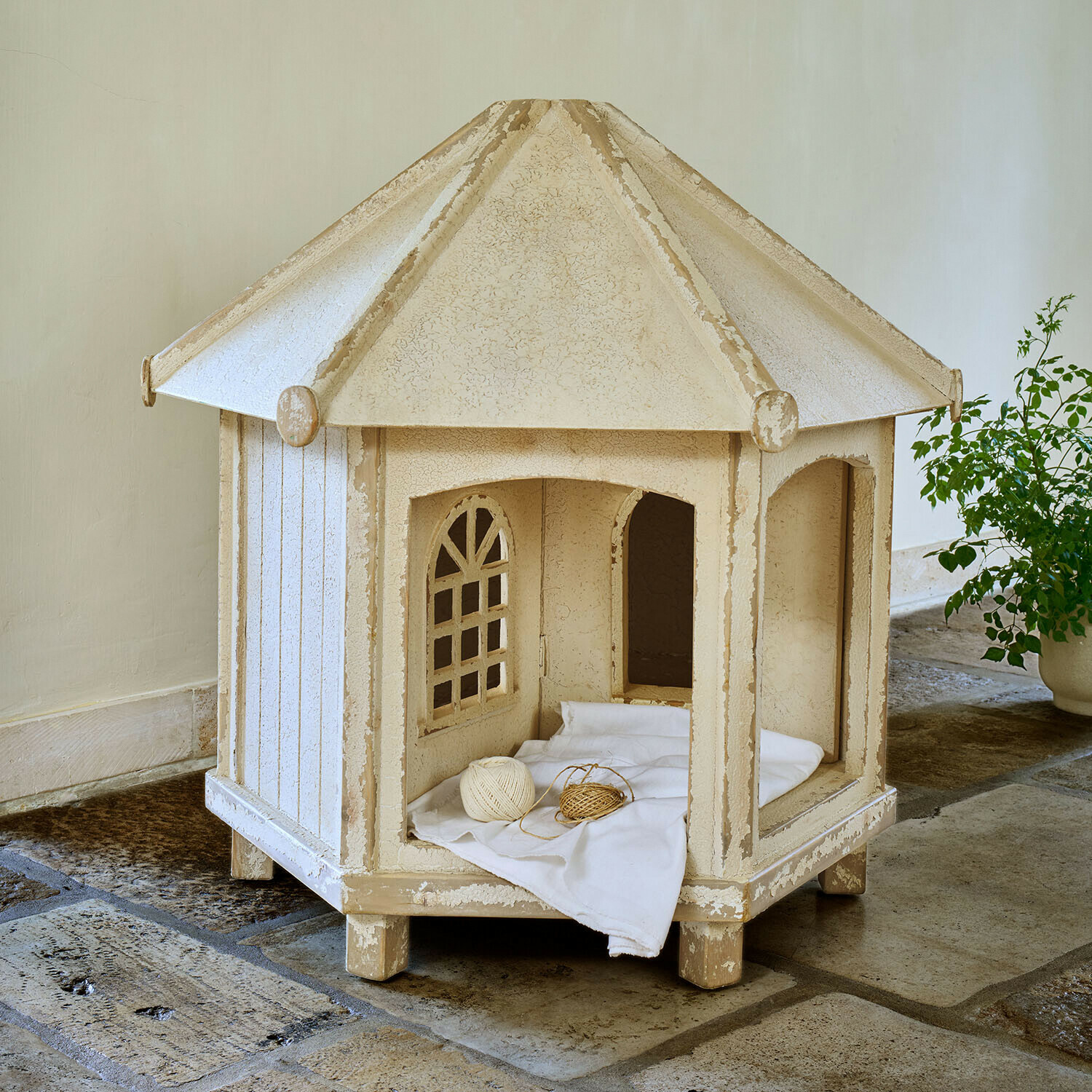 Maison pour chat en bois beige avec fenêtres et coussin blanc sur sol en pierre