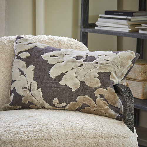 Coussin décoratif à motif de feuilles beige sur fond gris posé sur un fauteuil crème, textile d'intérieur