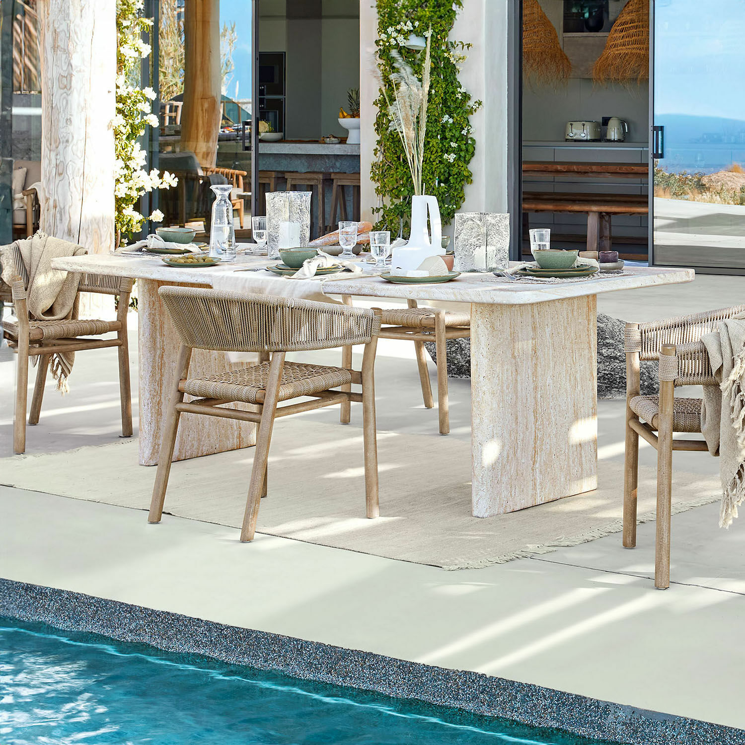 Table de salle à manger Yveline Table à manger en pierre claire avec chaises en bois tressé près d'une piscine dans une maison moderne