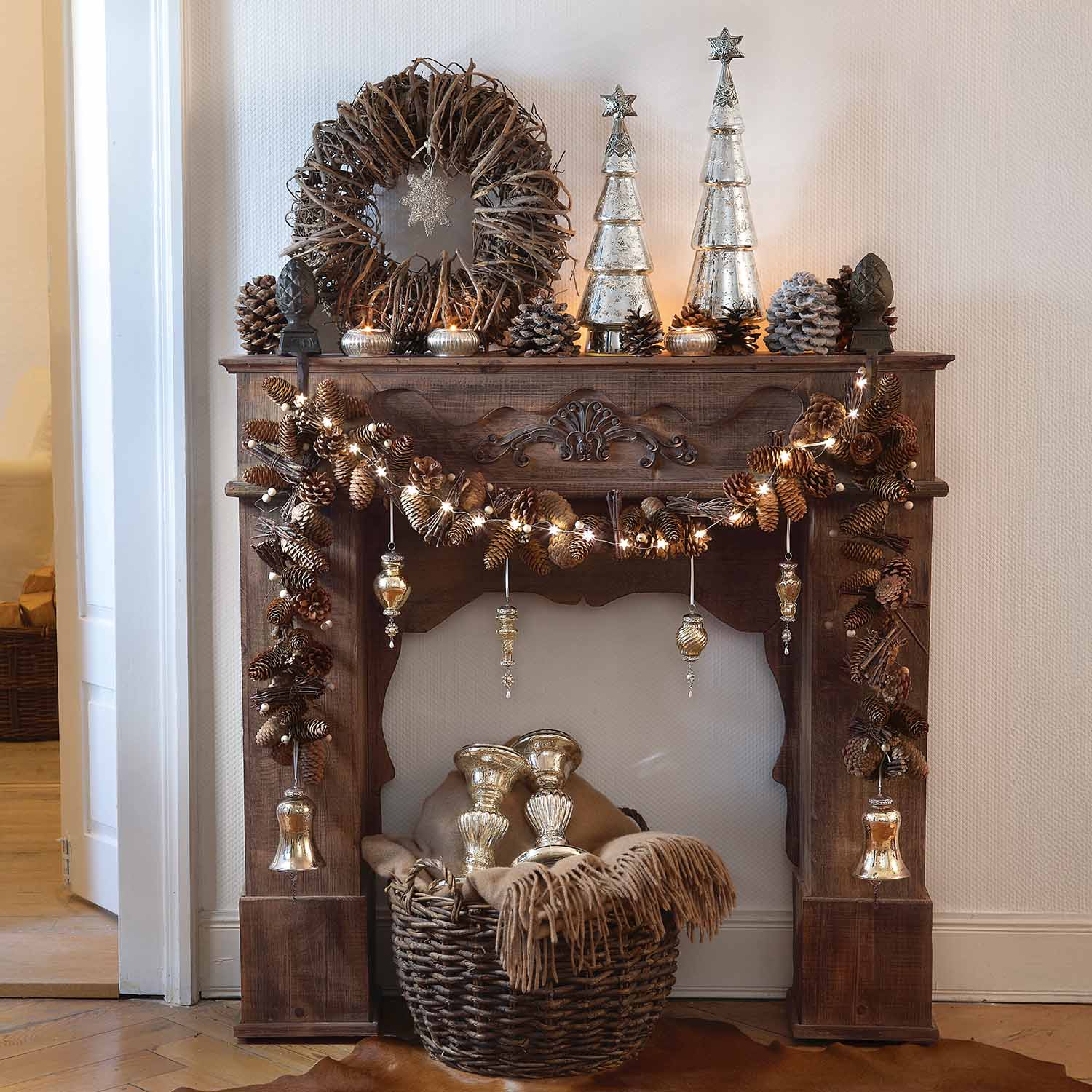 Cheminée en bois rustique décorée de pommes de pin, guirlandes lumineuses et ornements argentés de Noël