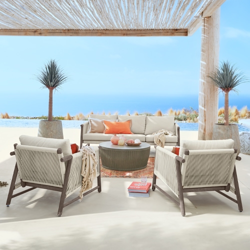 Ensemble de mobilier d'extérieur avec coussins beige et structure en bois sous une pergola face à la mer