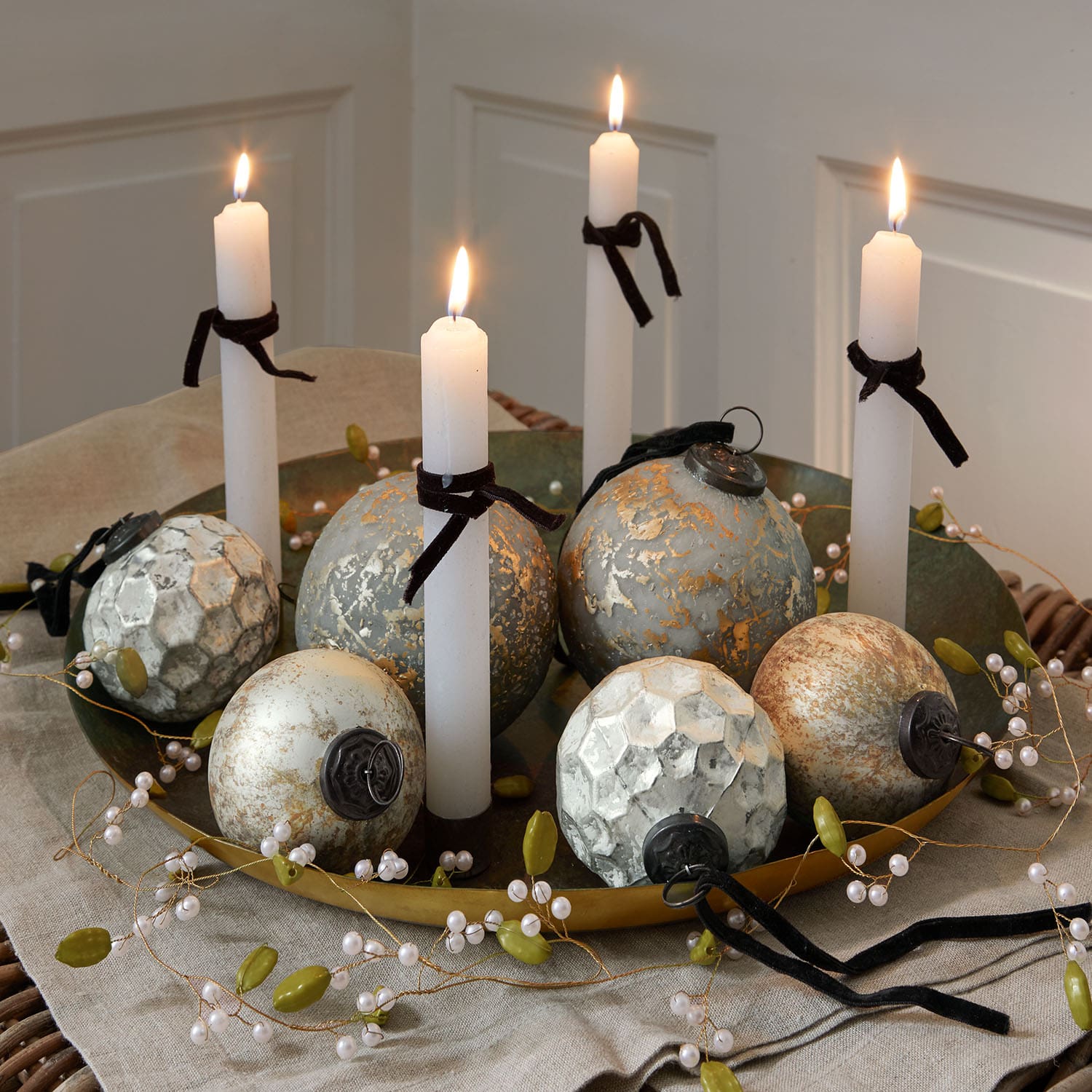 Plateau doré décoratif avec bougies blanches et boules métalliques vintage sur nappe en lin