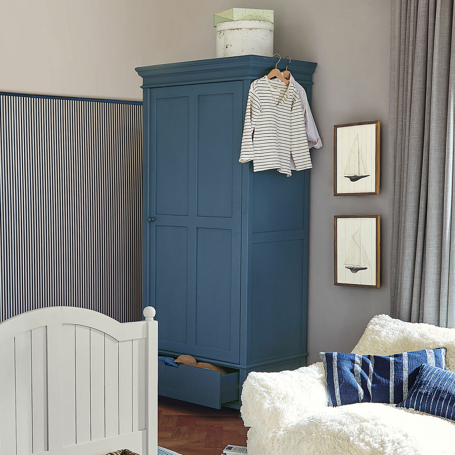 Armoire Westcombe Armoire en bois bleu marine avec tiroir ouvert et vêtements suspendus dans un salon cosy avec canapé blanc