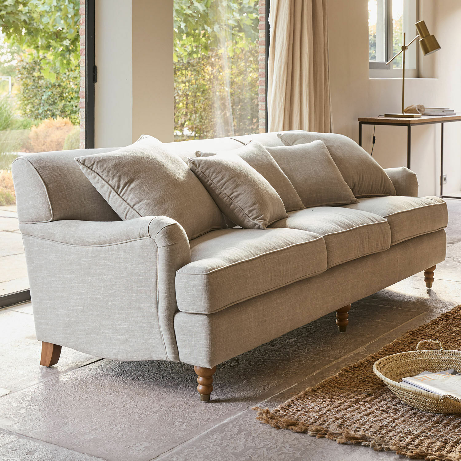Canapé Isa Canapé beige en tissu avec coussins et pieds en bois dans un salon lumineux avec tapis