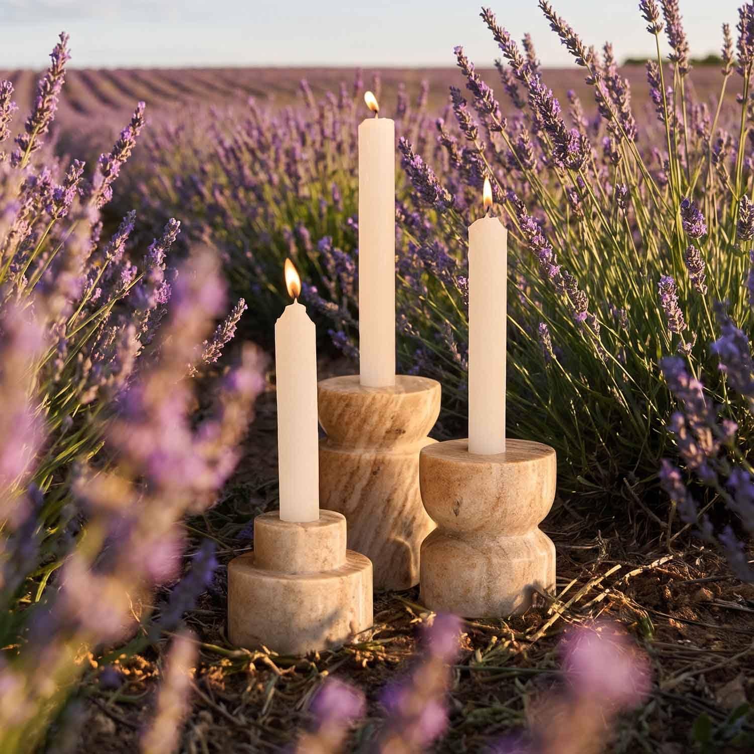 Trois bougies crème dans des bougeoirs en bois naturel au milieu d'un champ de lavande au coucher du soleil