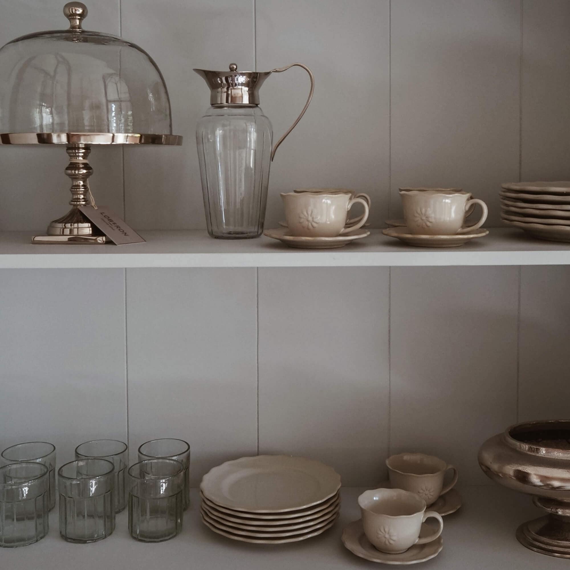 Ensemble de vaisselle crème avec tasses et assiettes, pichet en verre avec poignée métallique sur étagère