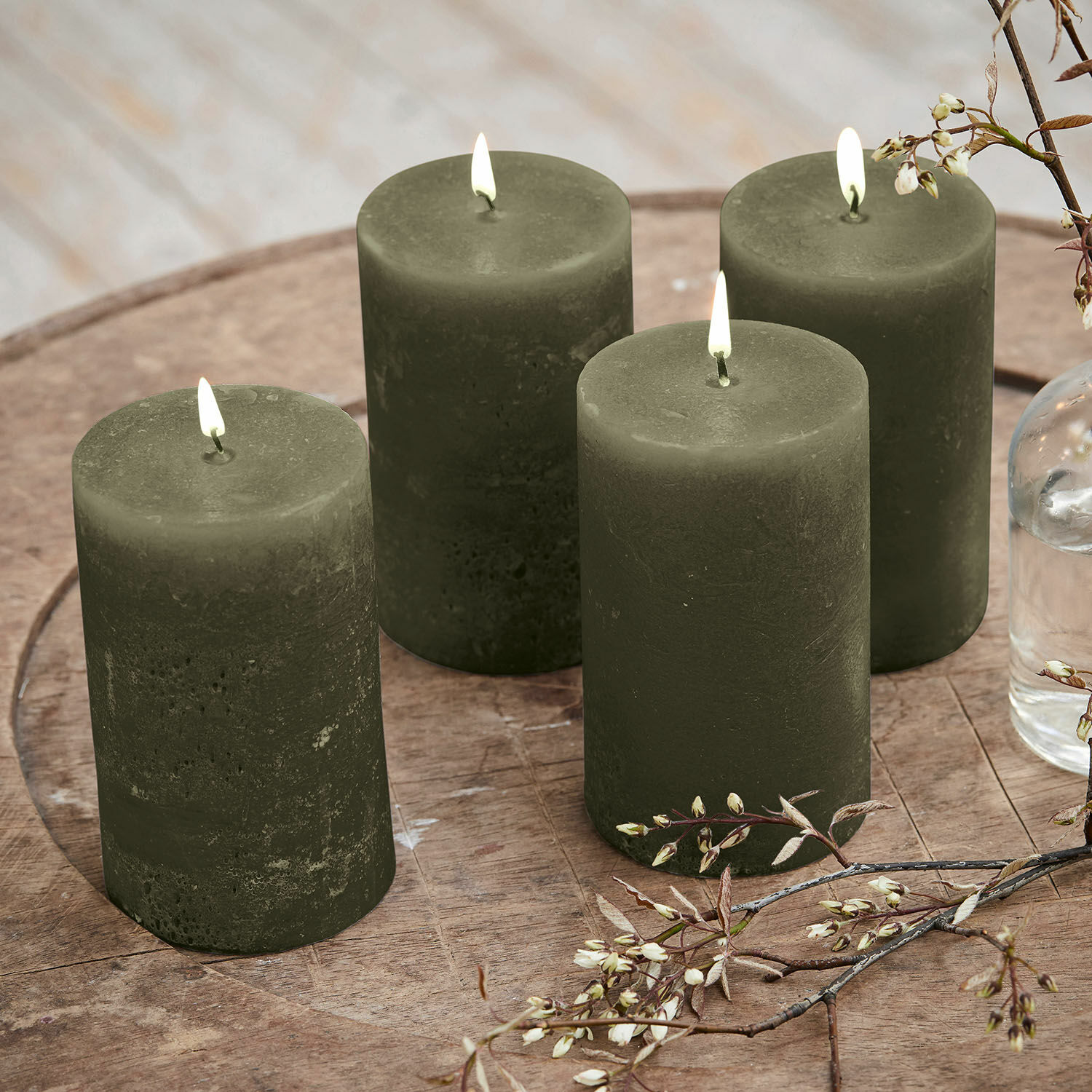 Lot de 4 bougies Braga Ensemble de quatre bougies vertes en cire sur une table en bois avec décoration florale