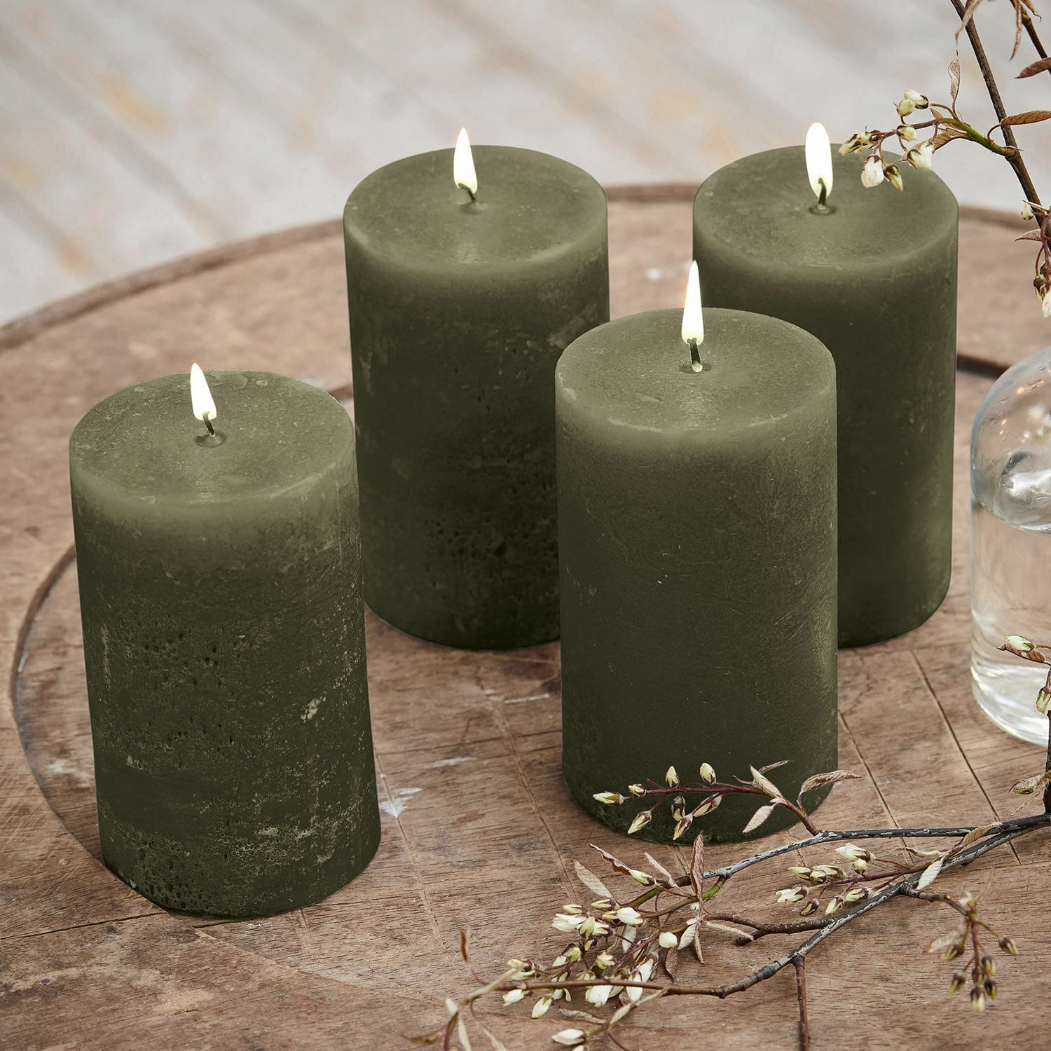 Lot de 4 bougies Braga Ensemble de quatre bougies vertes en cire sur une table en bois avec décoration florale