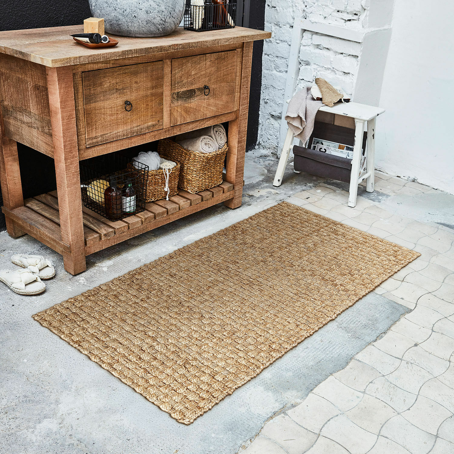 Tapis long Daoukro Tapis en jute beige naturel posé sur un sol à côté d'un meuble en bois et d'un tabouret blanc