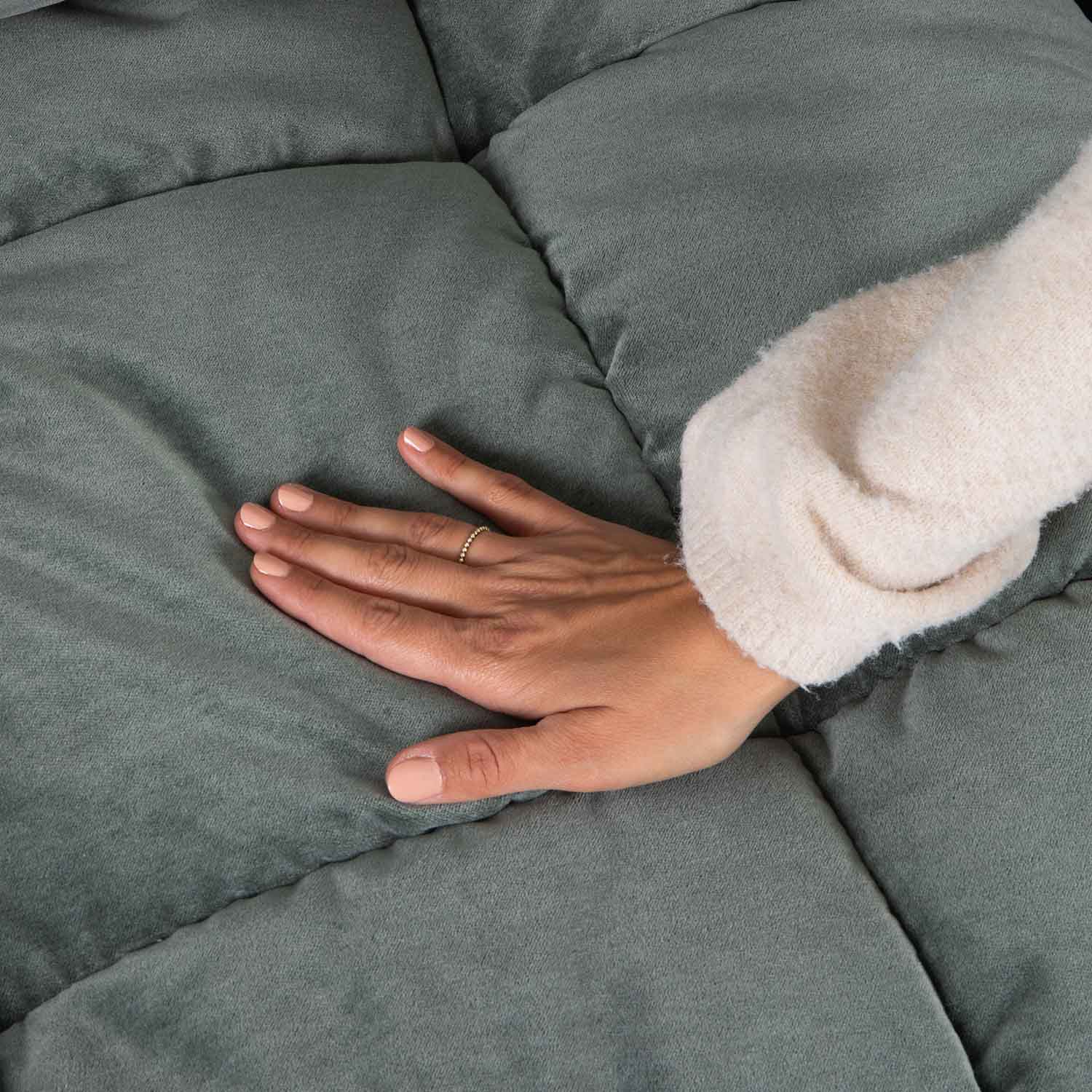 Main posée sur un tissu matelassé vert doux, illustrant la texture confortable et la qualité du textile