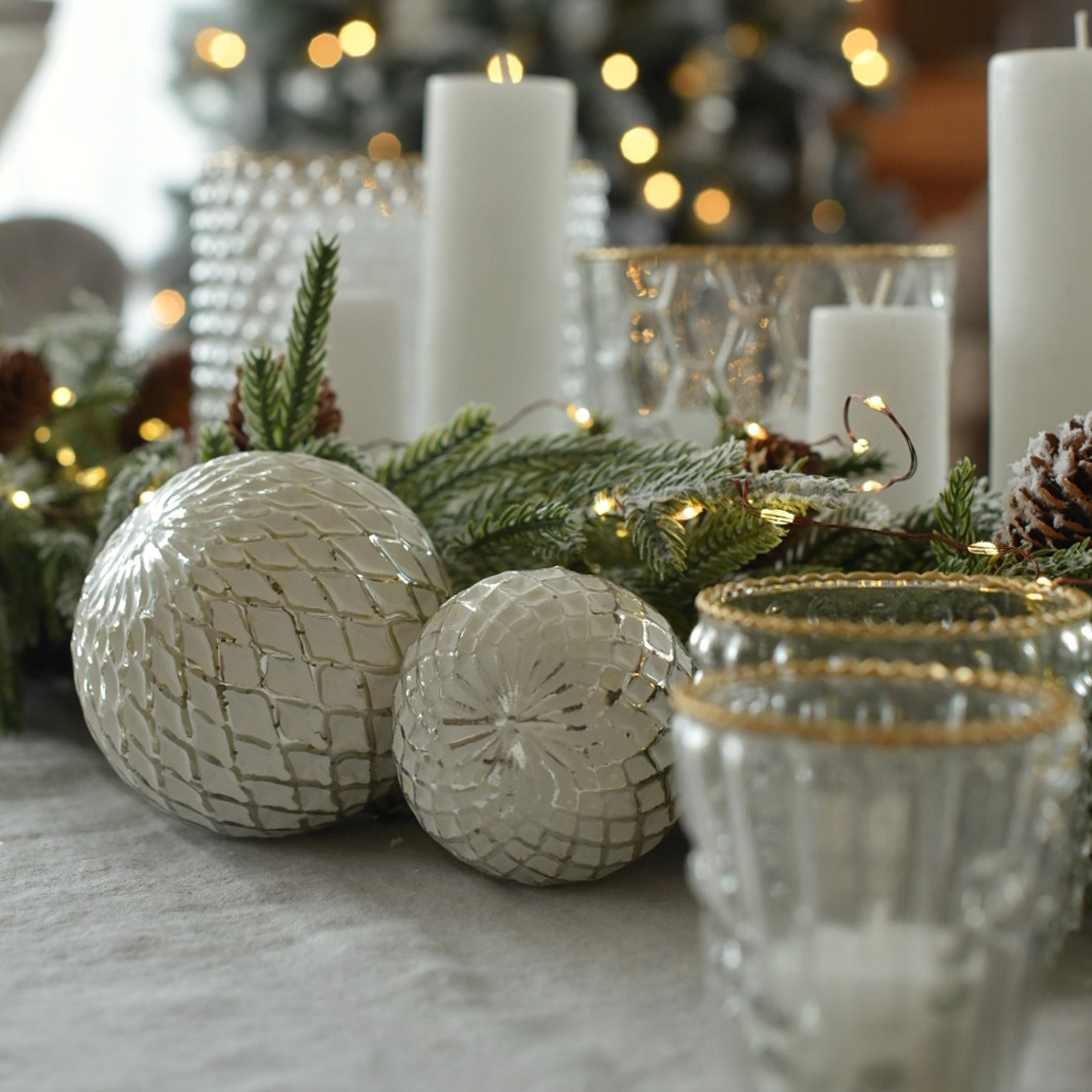 Boules décoratives blanches en verre avec motif losange sur table de Noël avec branches vertes et bougies