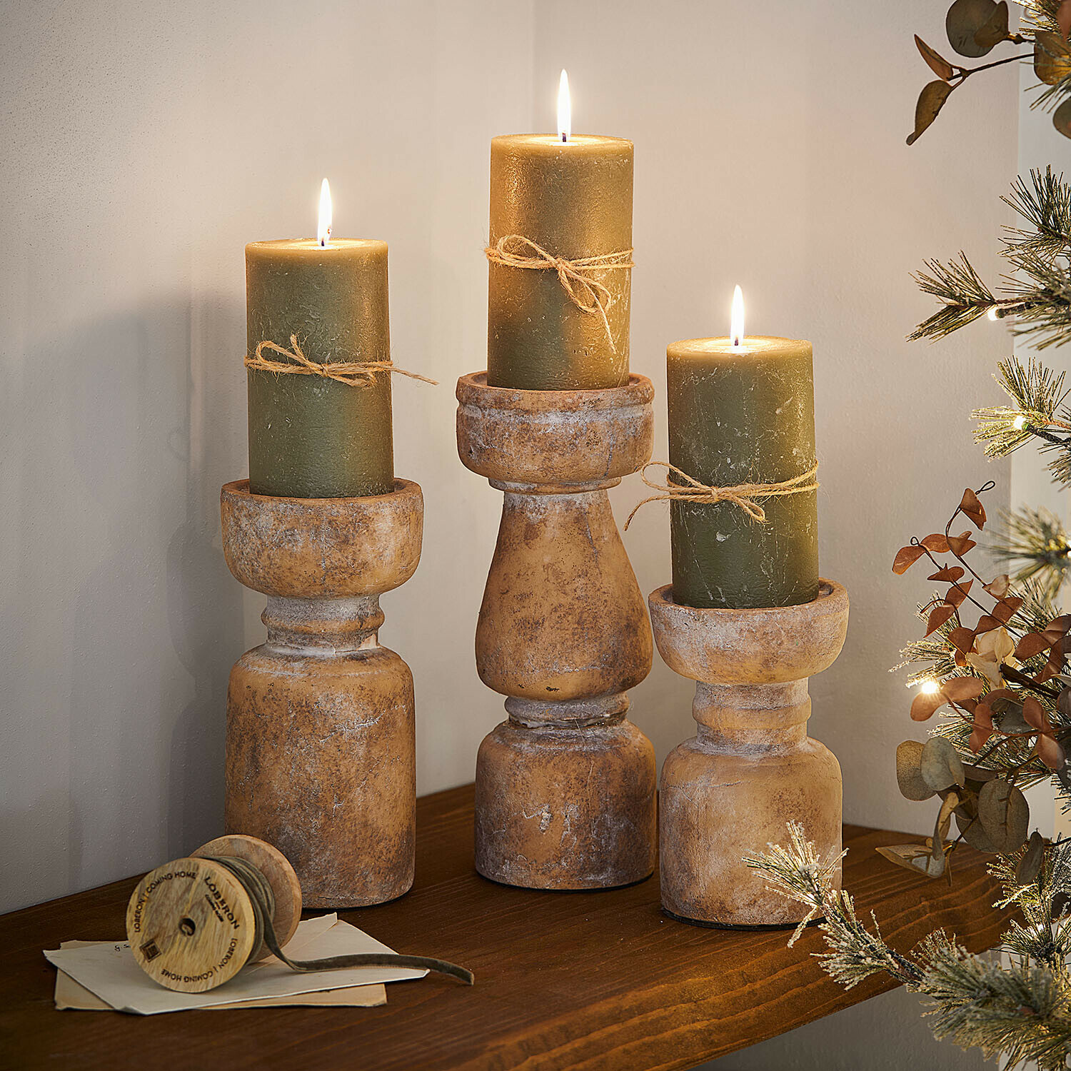 Set de 3 bougeoirs Talona Trois bougeoirs rustiques en bois avec bougies vertes et ficelle sur une étagère en bois décorative