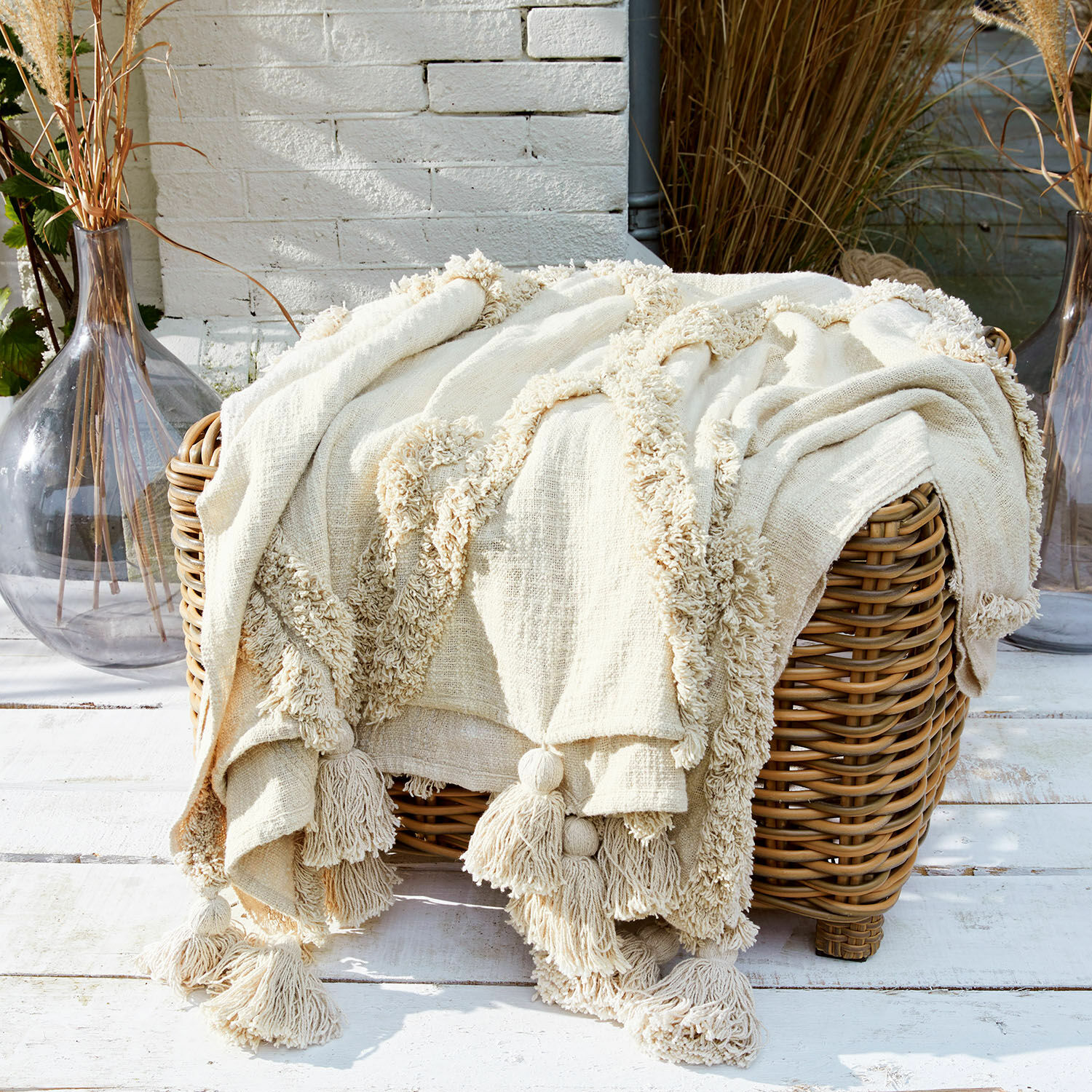 Plaid crème en coton avec pompons sur panier en osier, décoration intérieure et confort