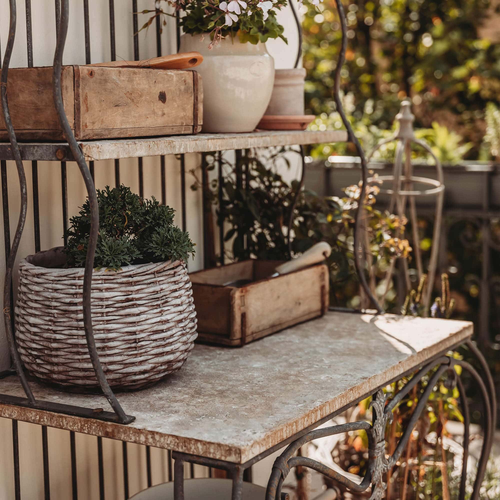Étagère en métal avec plateau en pierre et panier en osier contenant une plante verte sur la terrasse