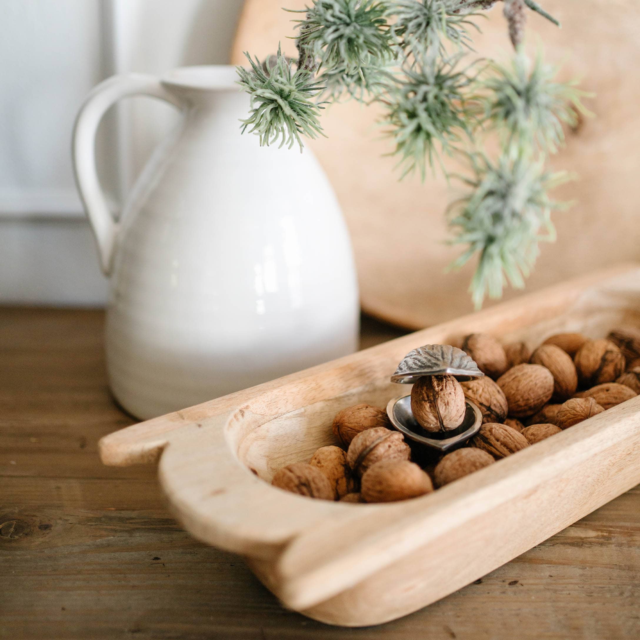 Plateau en bois avec noix et casse-noix en métal sur table en bois avec cruche blanche