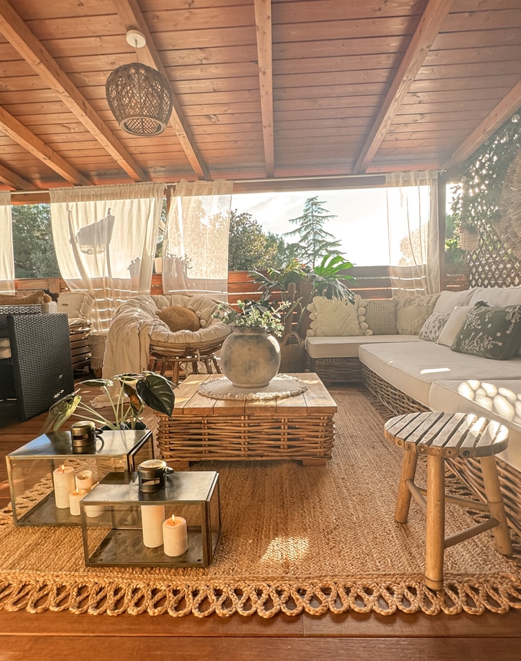 Terrasse cosy avec meubles en rotin, coussins clairs et tapis naturel en jute sous lumière douce