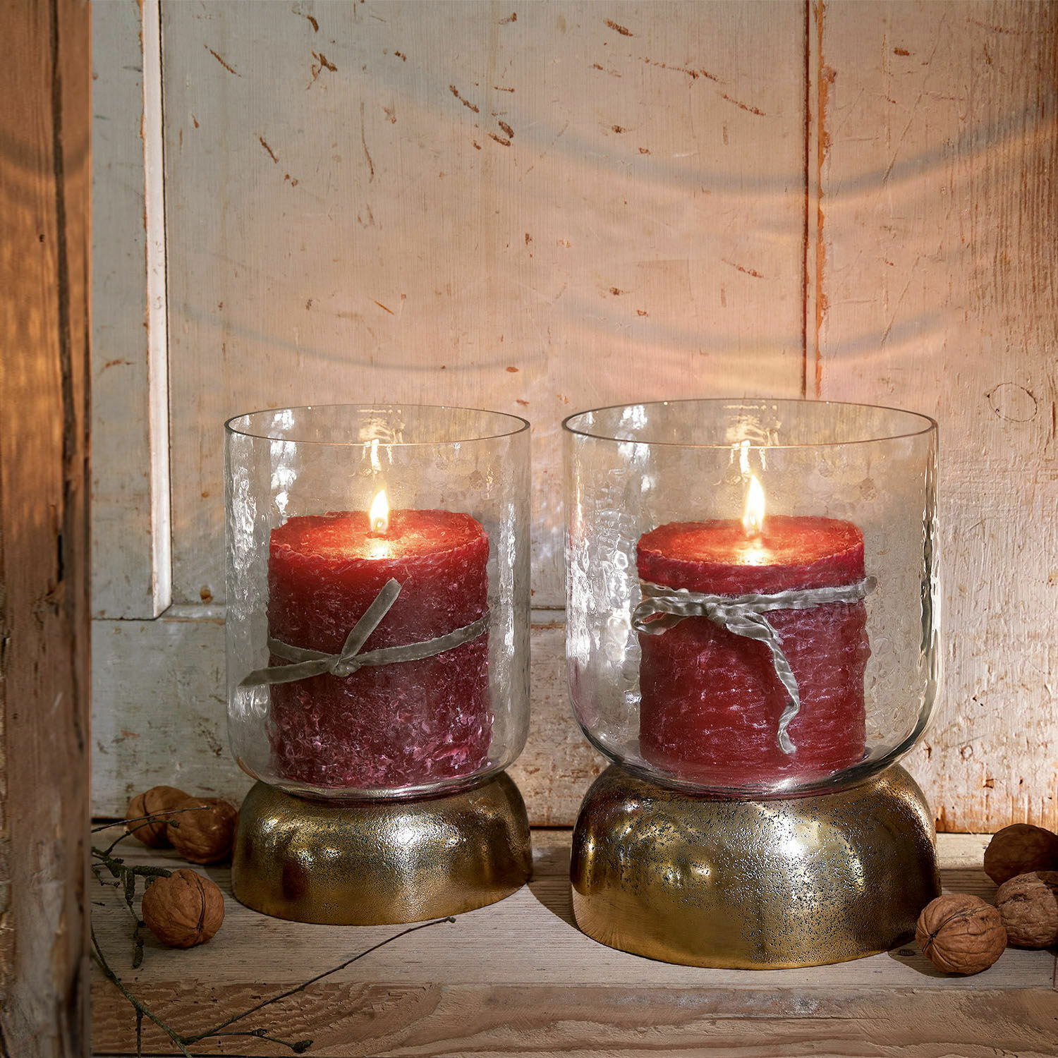 Lot de 2 photophores Biserre Deux bougies rouges dans des verres avec socles dorés sur fond en bois rustique