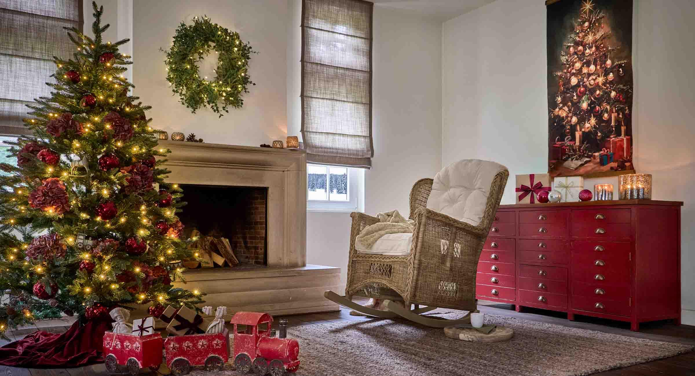 Salon chaleureux avec sapin de Noël, fauteuil en osier et buffet rouge décoré pour les fêtes