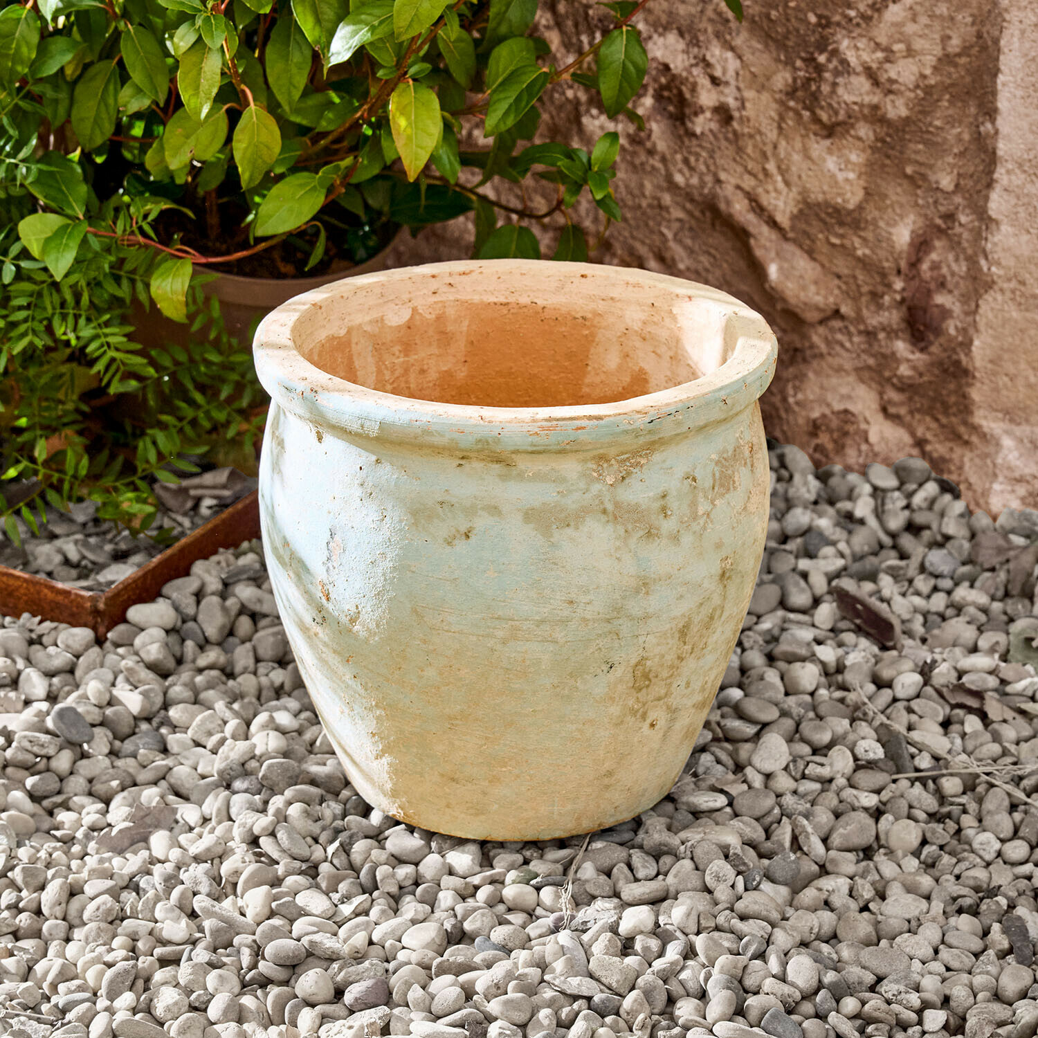Grand pot en céramique beige clair posé sur des cailloux dans un jardin extérieur